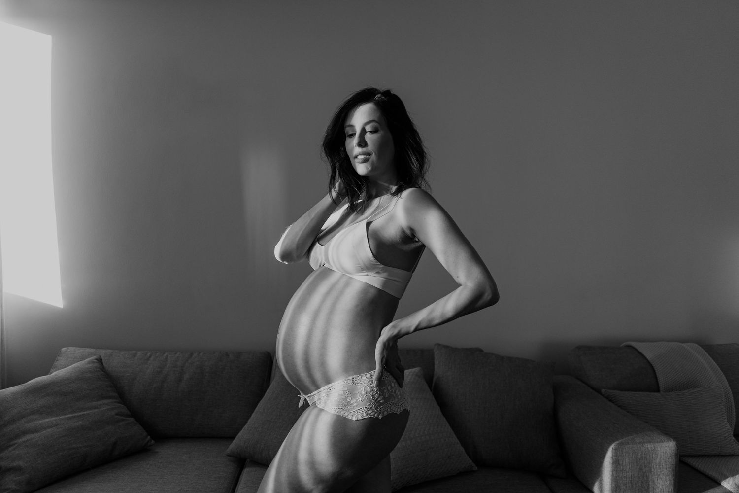 A maternity portrait in black and white showing a woman posing on a couch.