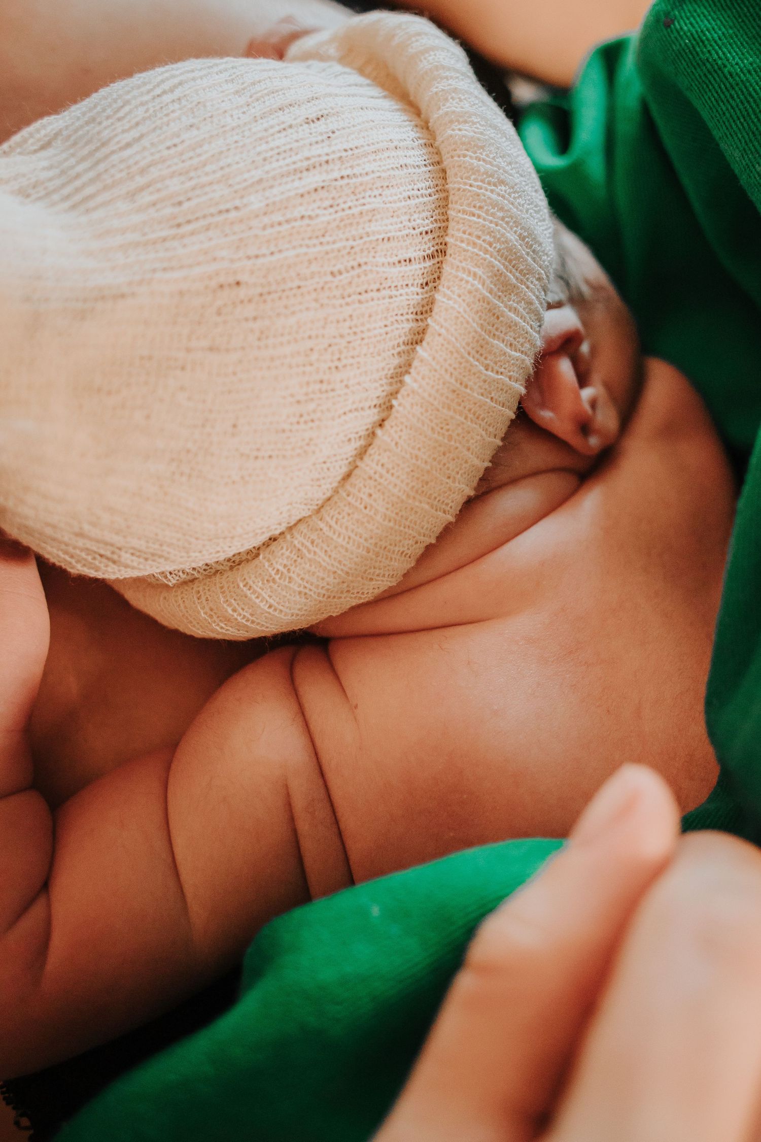 Close-up of newborn wearing white knit cap nestled against green hospital fabric.