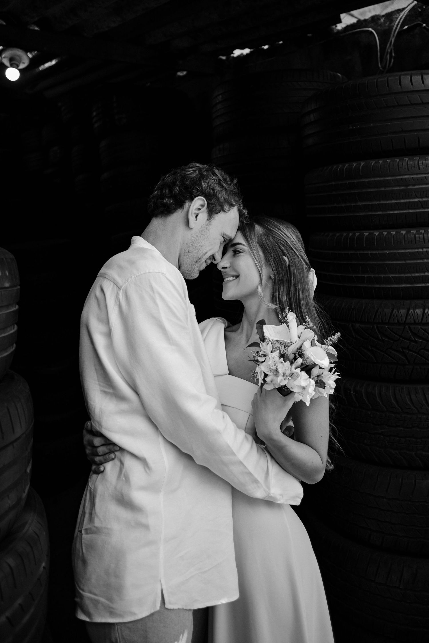Newlyweds embracing and smiling while holding a bouquet in an industrial setting.