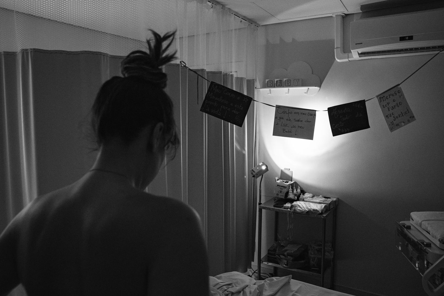Silhouette of a person looking at photos hanging from string lights in a dim room.