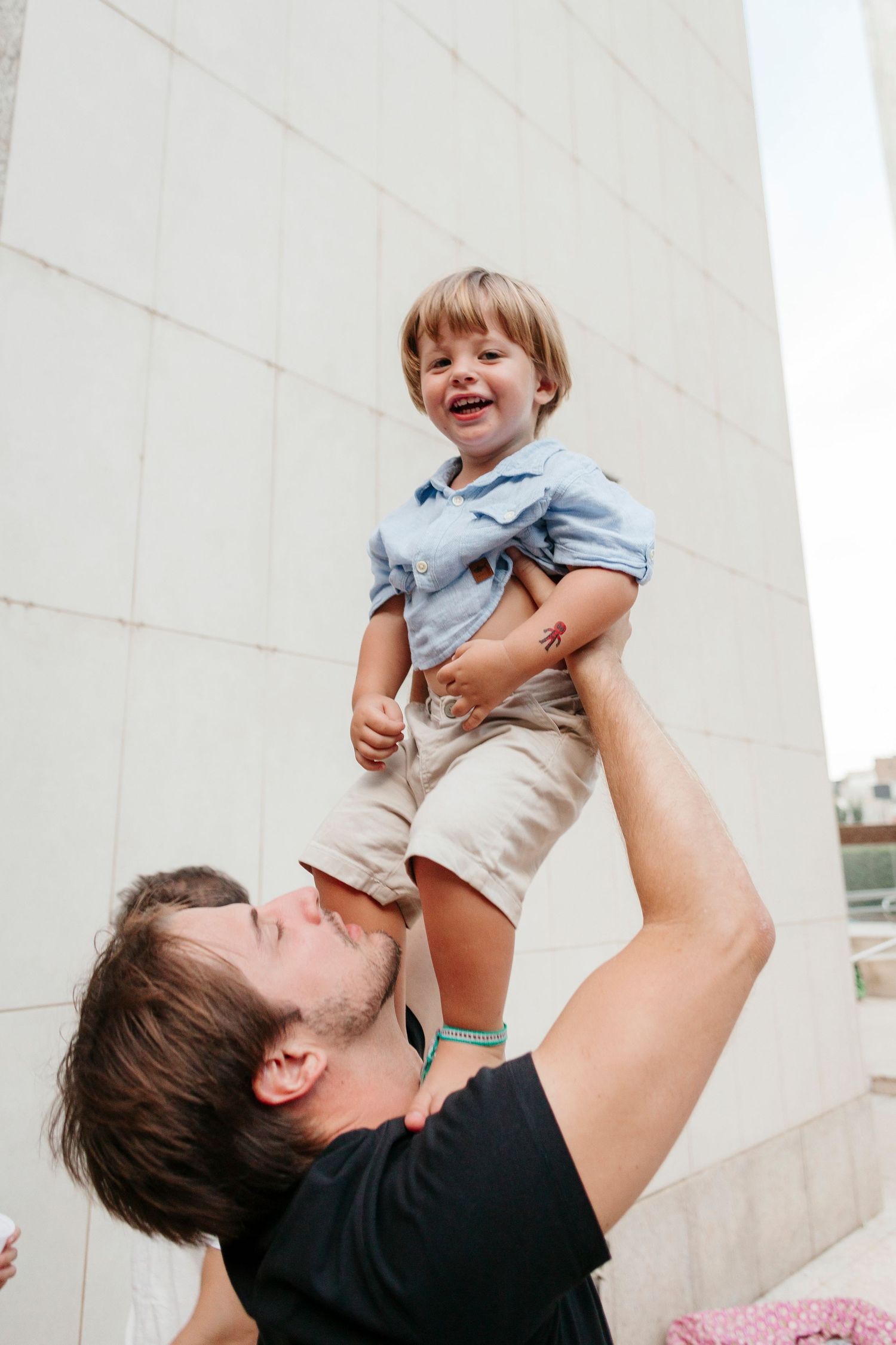Parent lifting happy child wearing light blue shirt and khaki shorts high in the air.