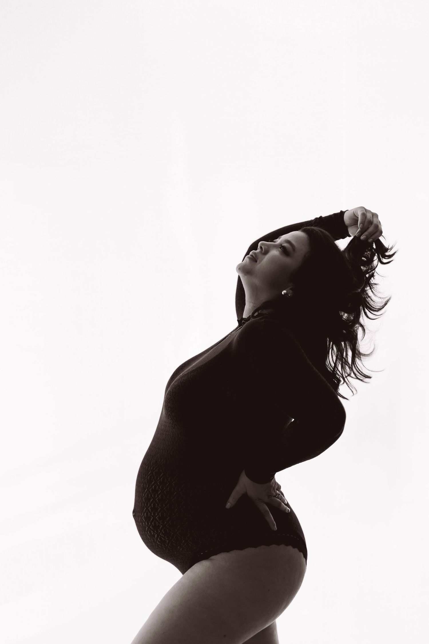 Black and white silhouette of pregnant woman in bodysuit posing gracefully against white background.