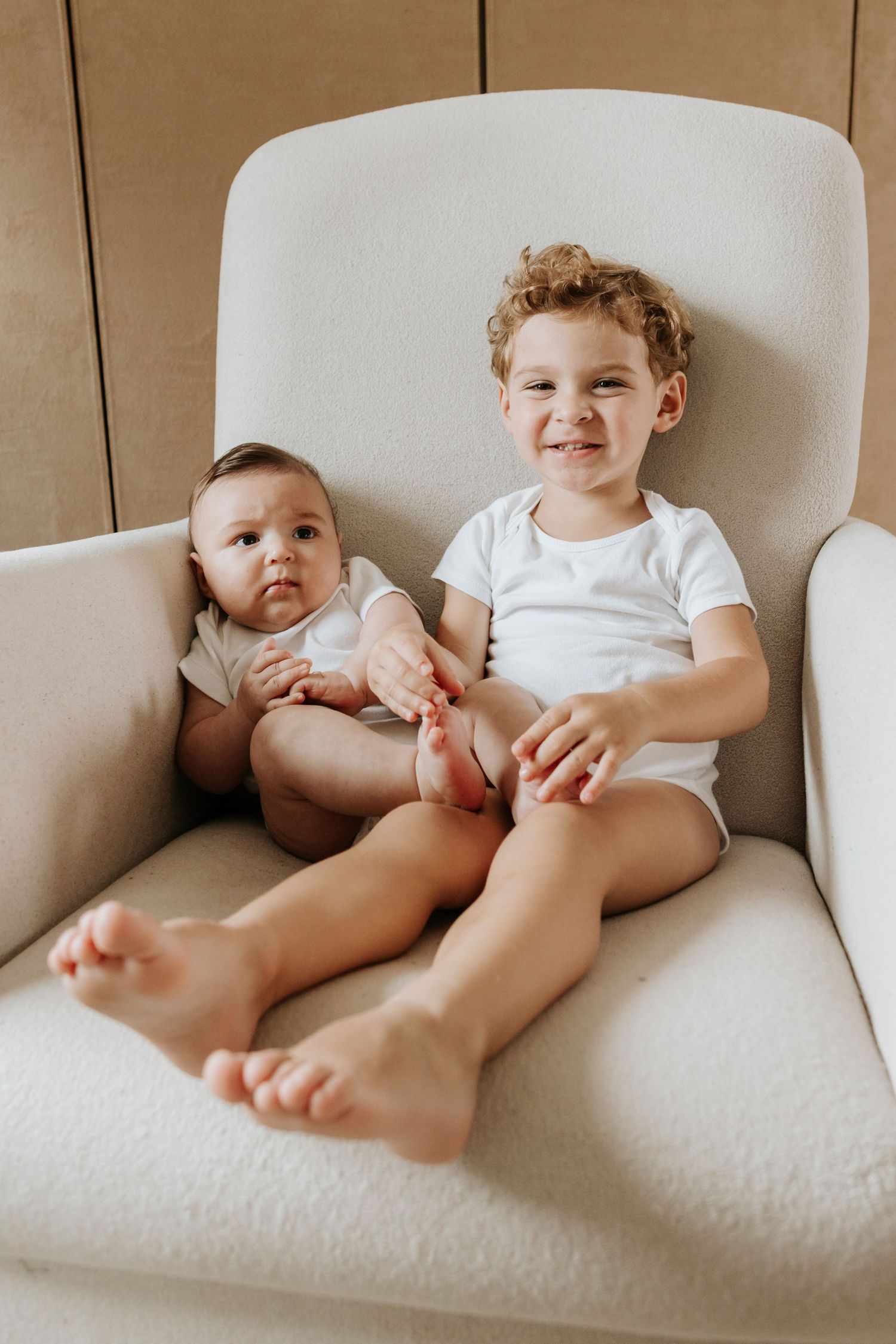 Four sequential photos of siblings lying on a cream colored couch showing playful interaction between them.