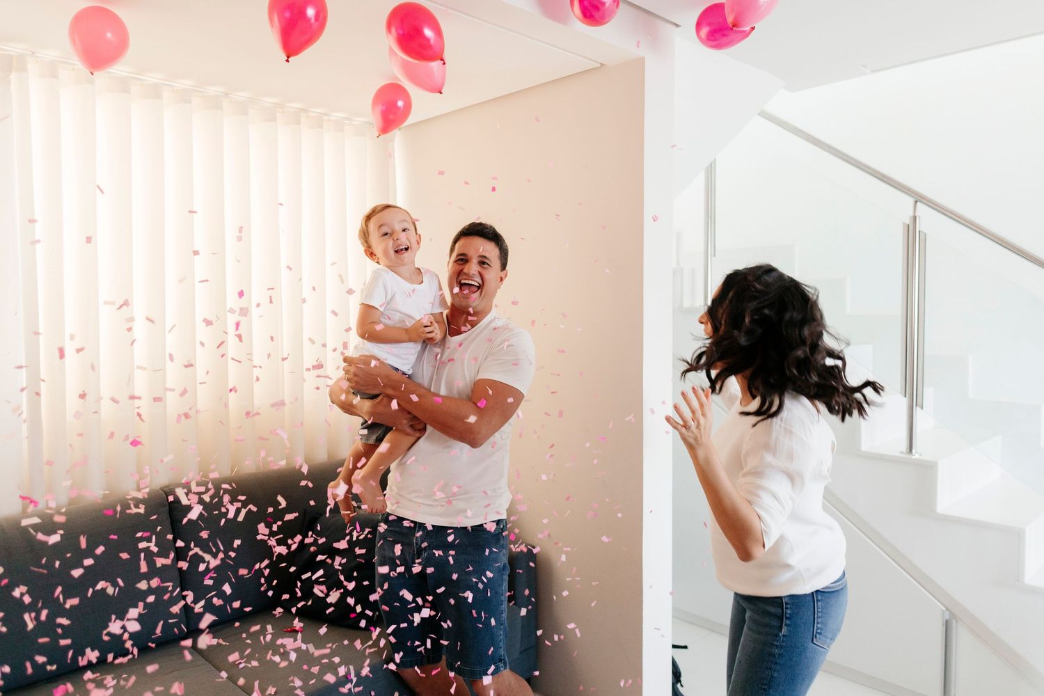 A joyful celebration scene with pink balloons and confetti in a bright white interior space.