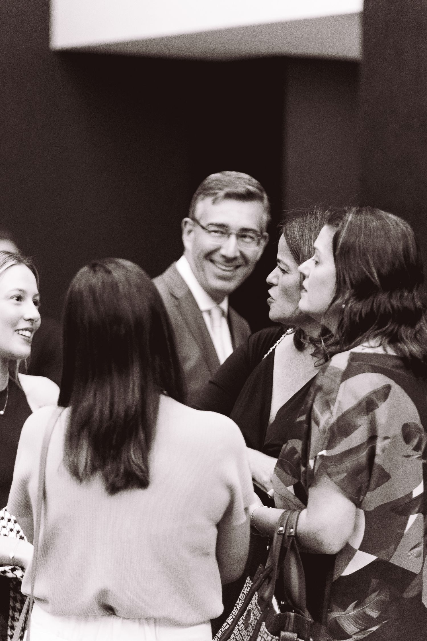 A group of people engaged in lively conversation at a social gathering, captured in black and white.