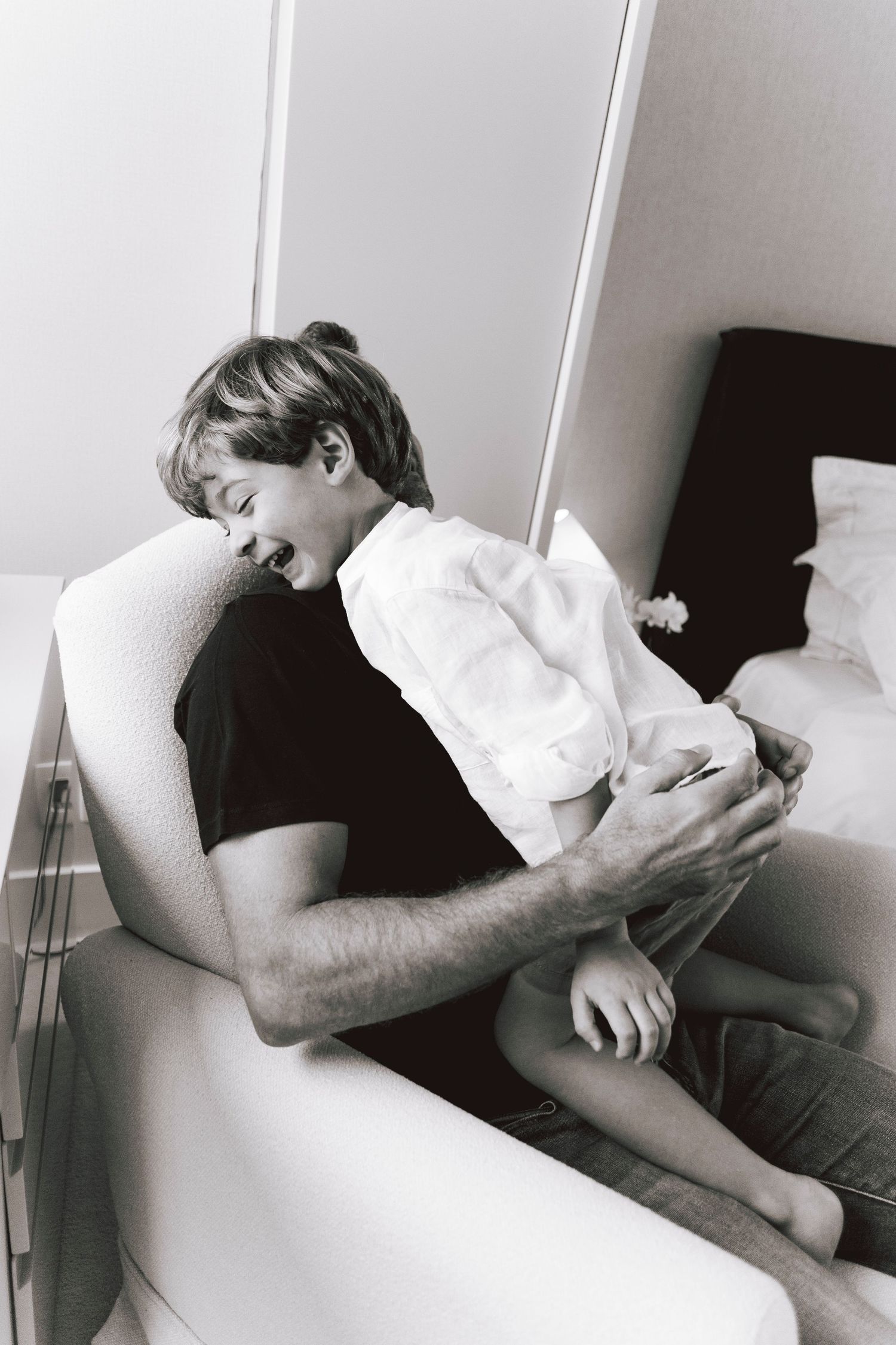 Intimate black and white moment of parent and child cuddling on white chair.