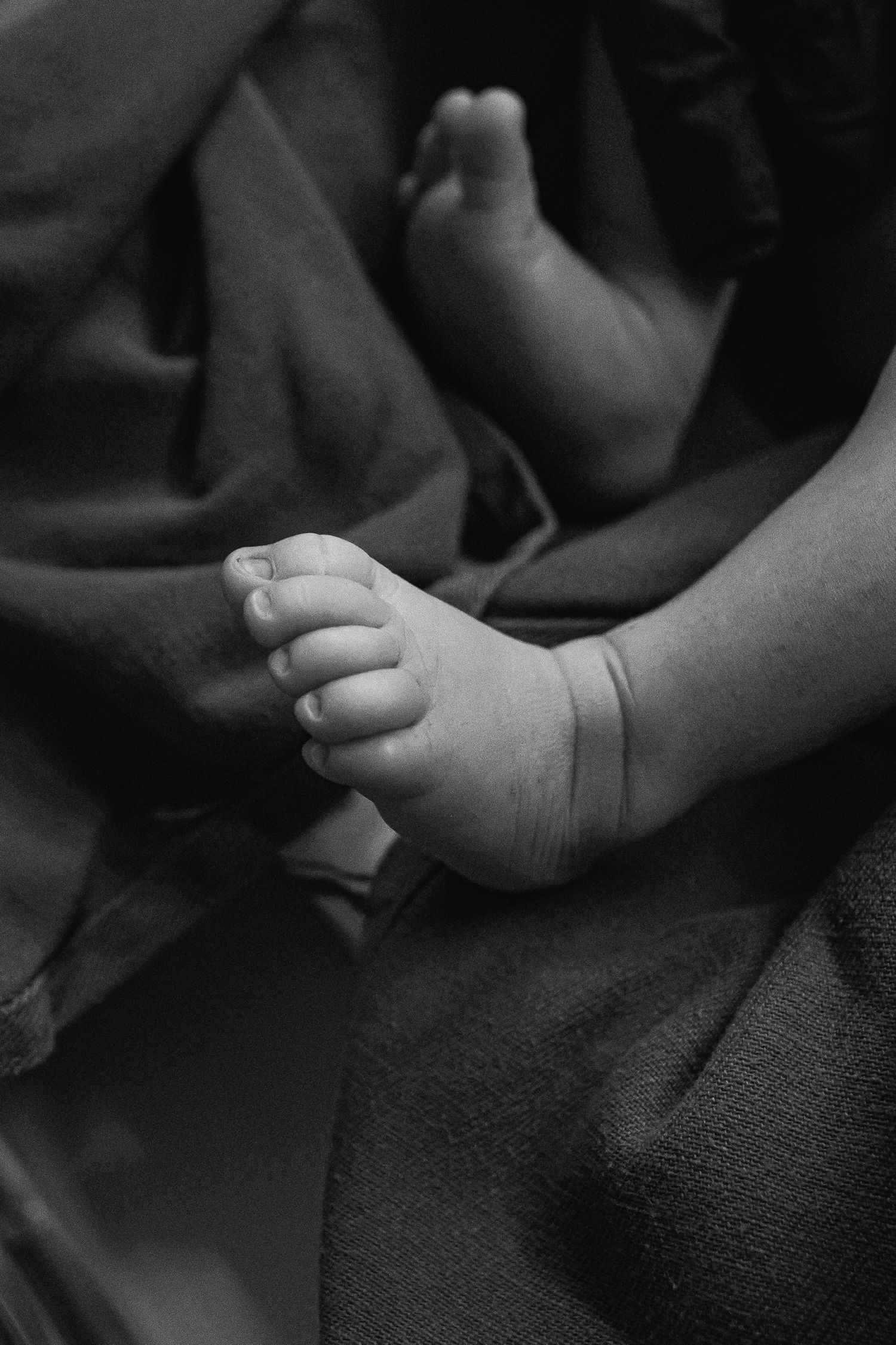 Close-up black and white photograph of a baby's small foot resting on dark fabric.