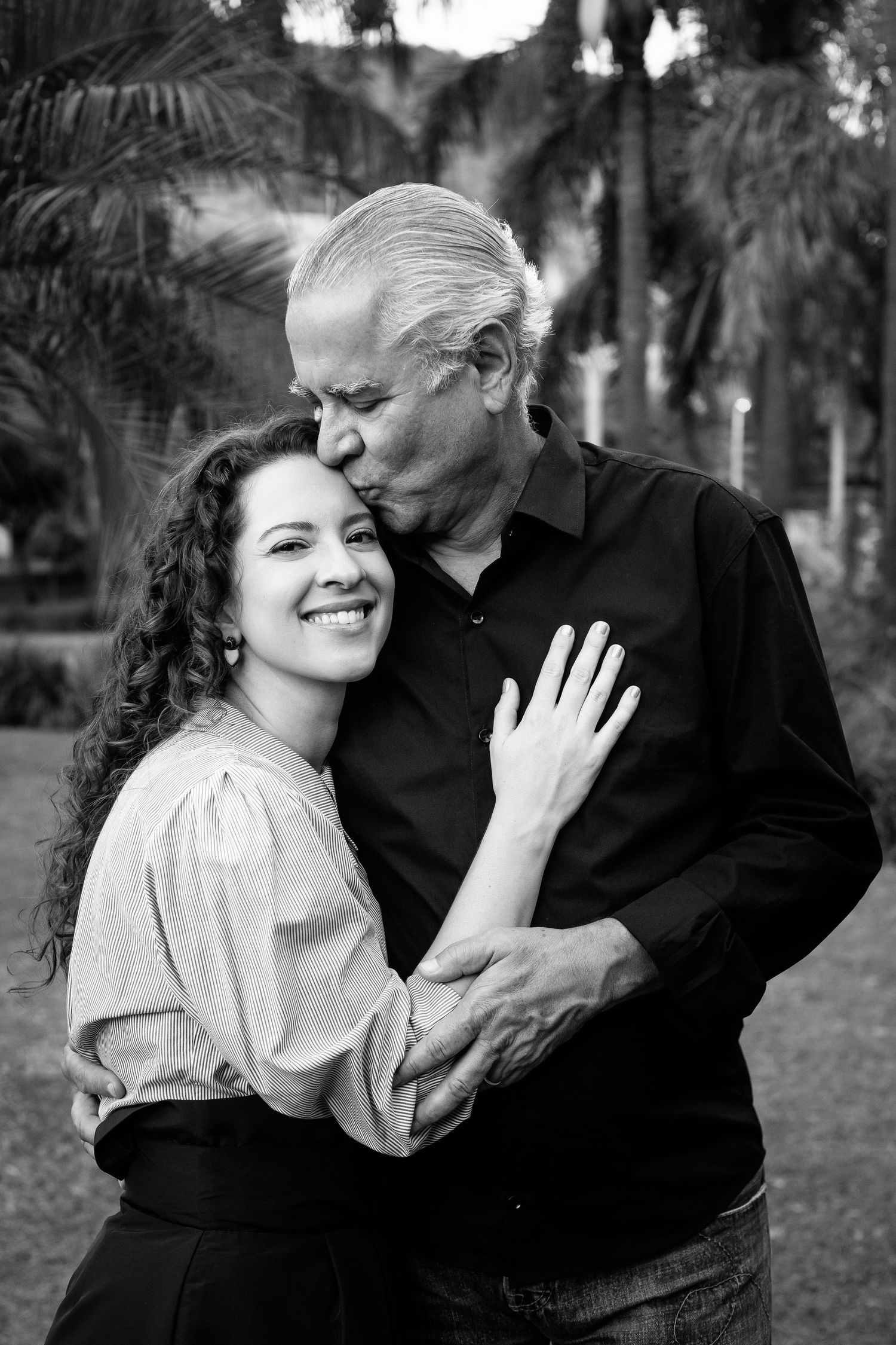 A tender black and white portrait of a couple embracing outdoors with tropical plants in background.