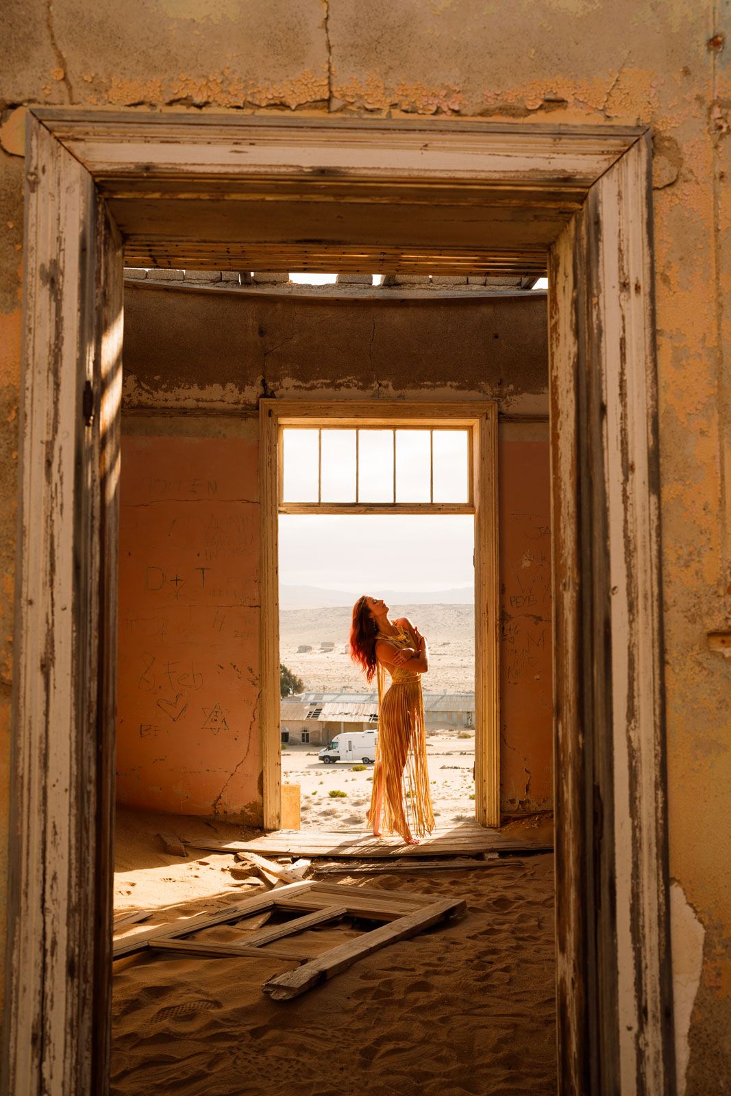 Figure silhouetted in abandoned building doorway with desert view.