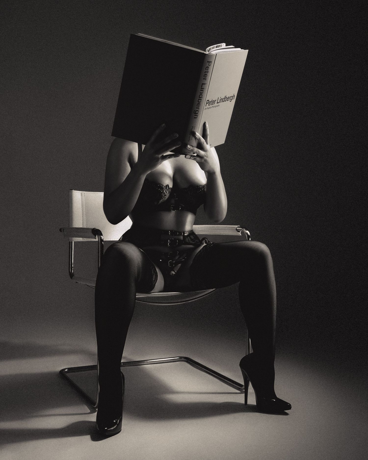 Artistic black and white photo of person in lingerie reading book on chair.