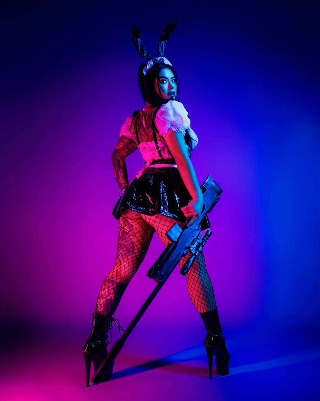 Cosplay photo with neon lighting features bunny ears and prop gun creating dramatic atmosphere.