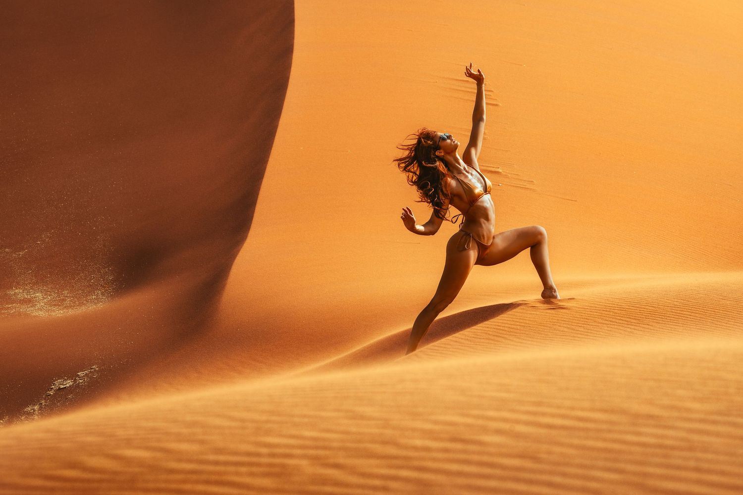 Dramatic dance pose captured against orange sand dunes in desert setting.