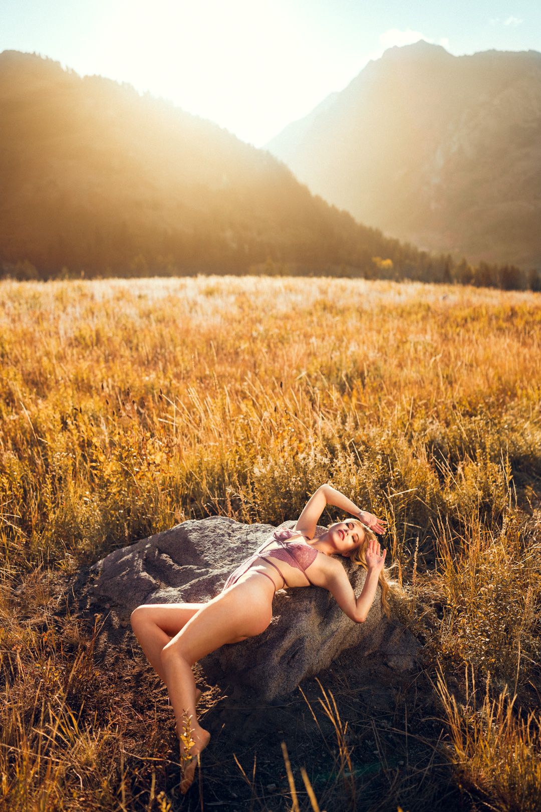 Figure lounging on rock in golden mountain meadow during sunset.