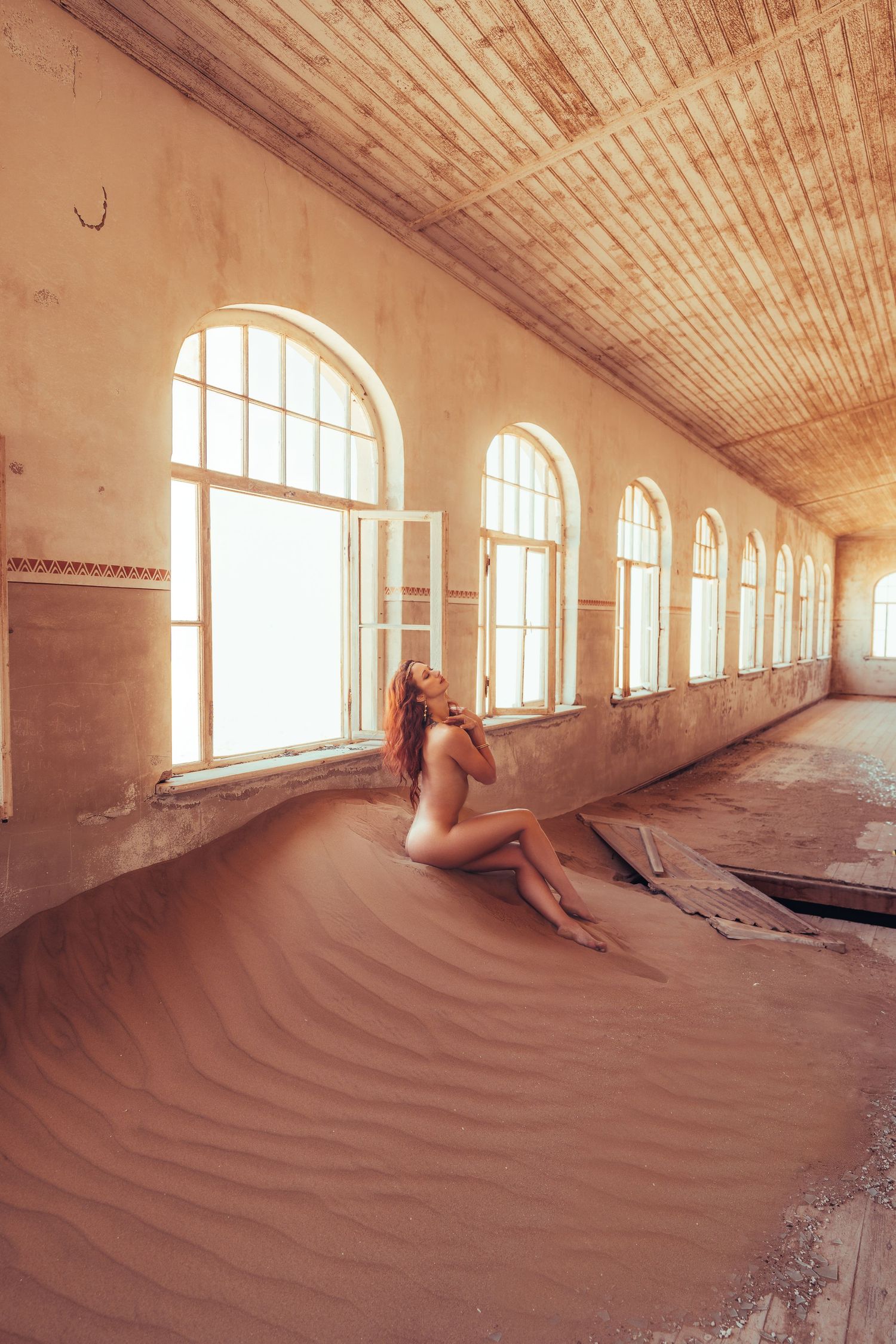 Sand dunes flow through abandoned building with arched windows letting in natural light.