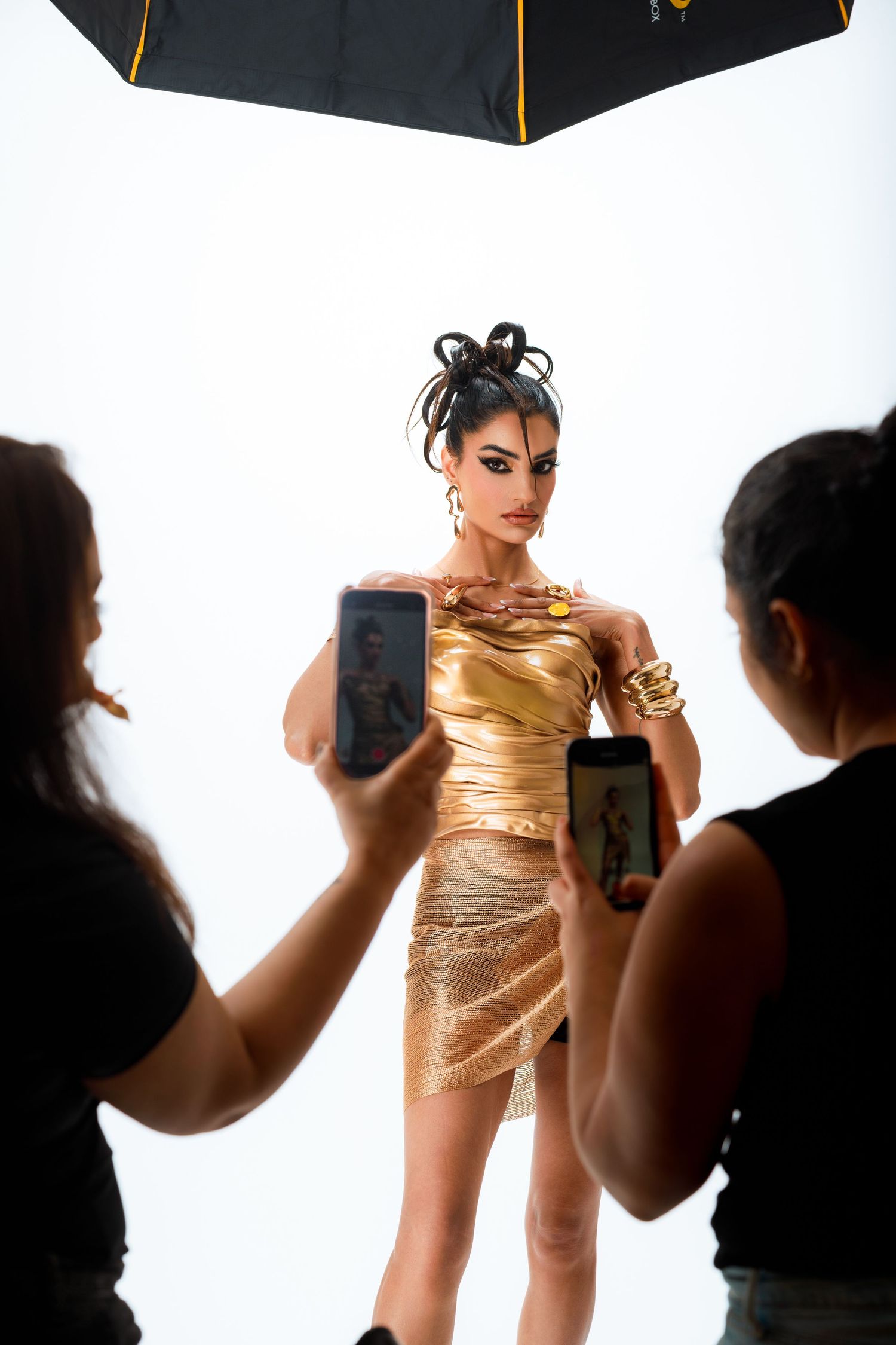 Behind-the-scenes photo of fashion shoot with photographers capturing model in gold dress.