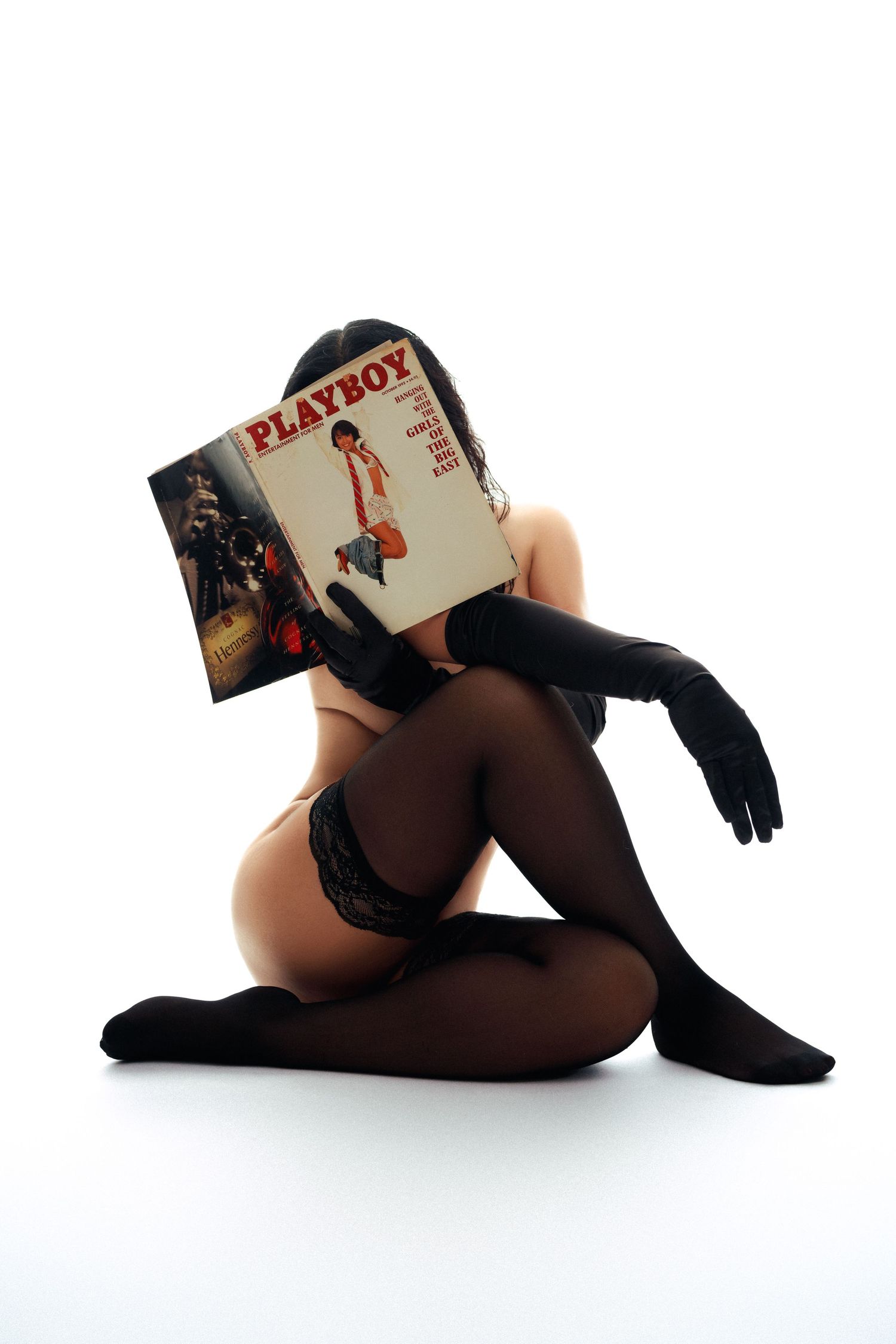 Artistic silhouette of model in black stockings holding vintage magazine in minimalist white setting.