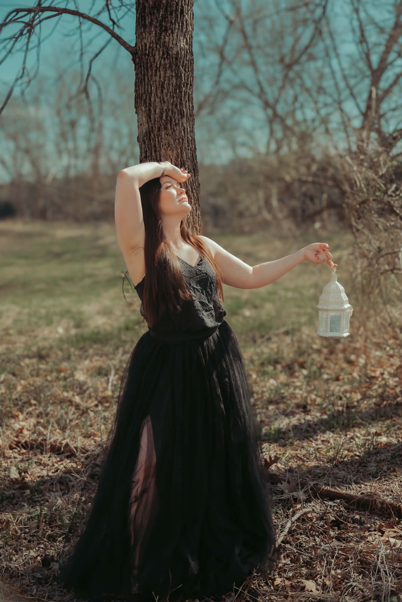 Woman with black flowy dress holding a prop lantern photographed in the fall woods.