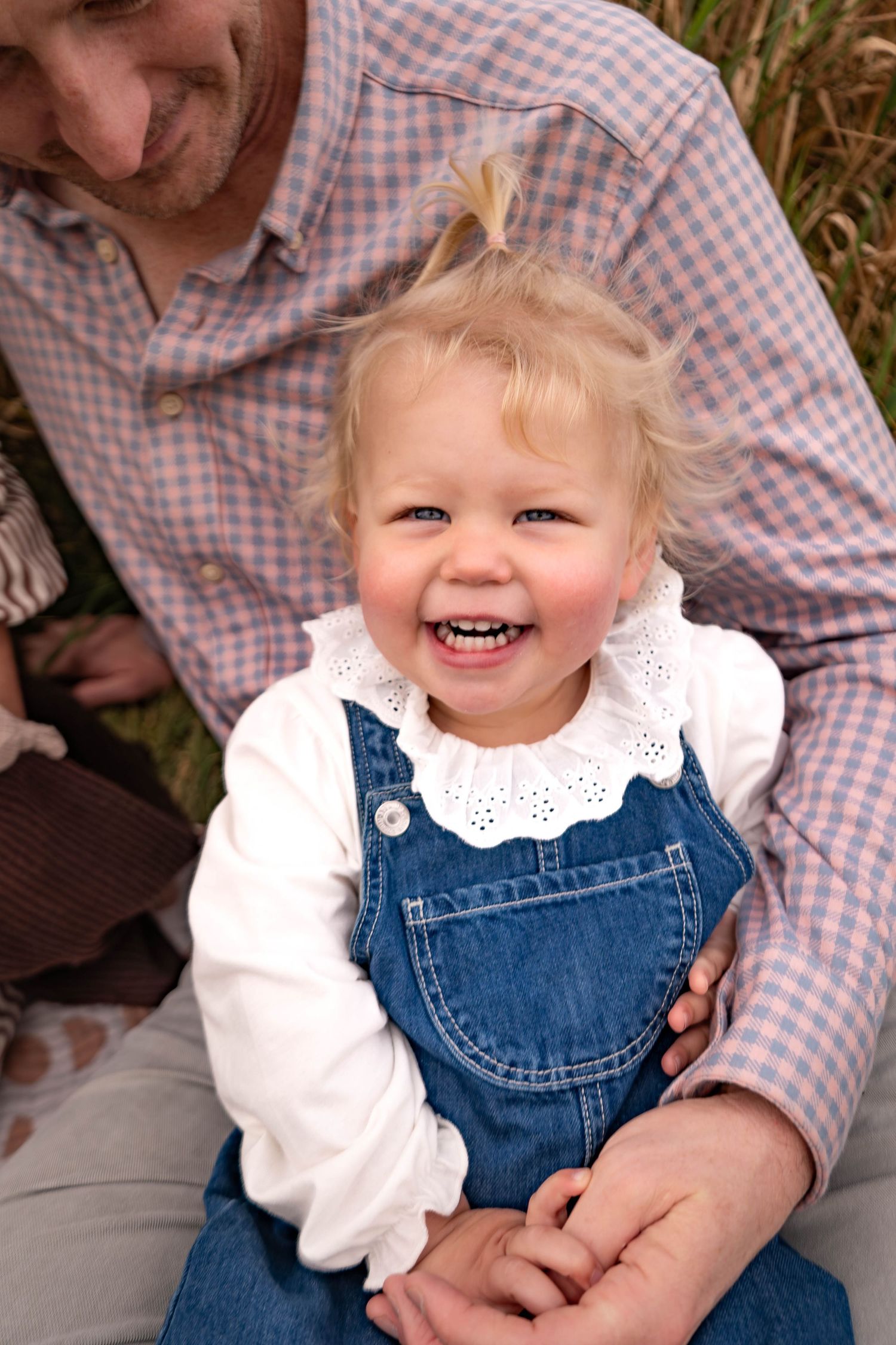 A sequence of joyful moments showing a child in denim overalls and white blouse sitting on someone's lap outdoors.