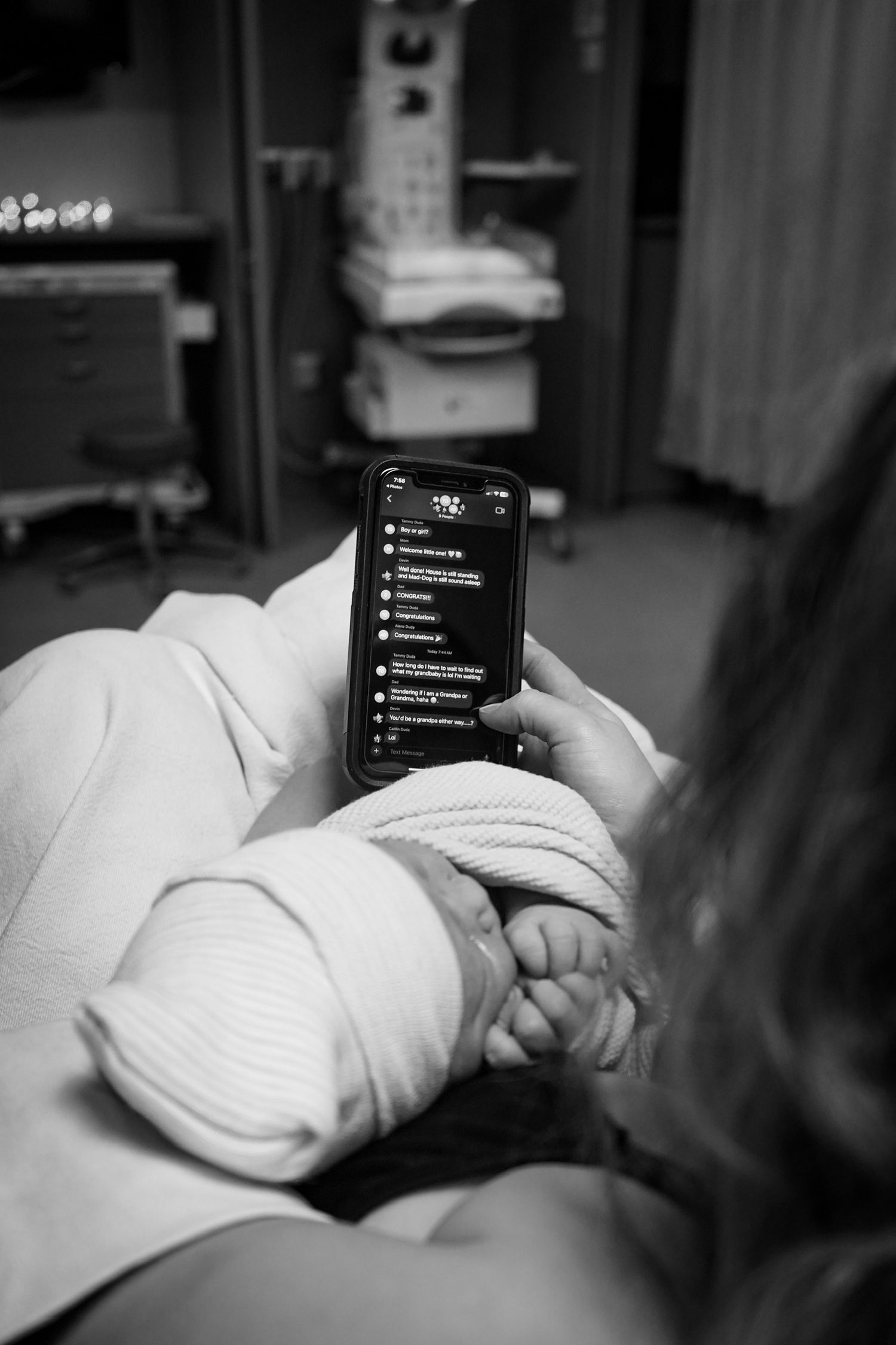 Black and white photo of person holding phone in hospital bed.