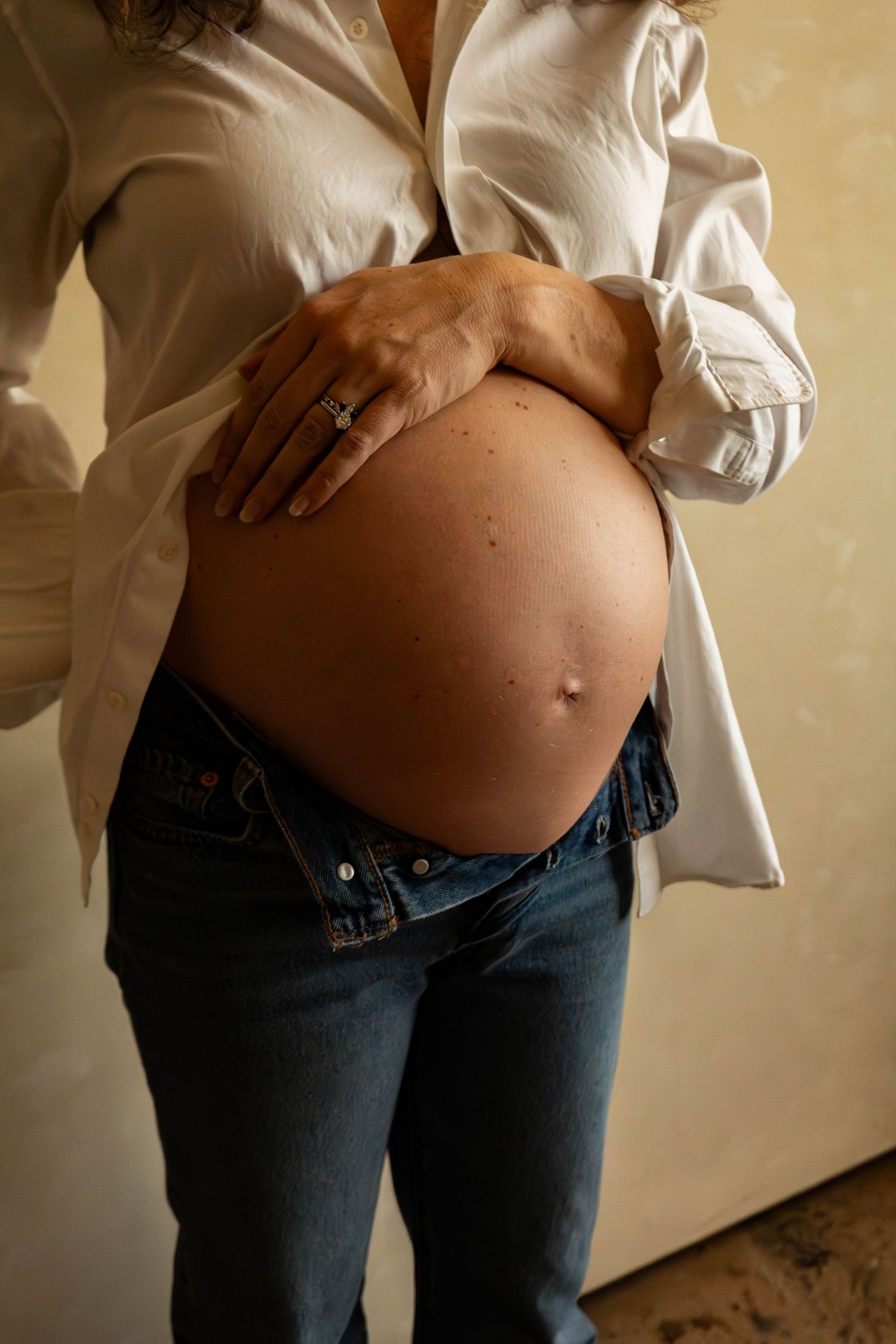 Artistic maternity series showing growing belly with casual white shirt and denim.