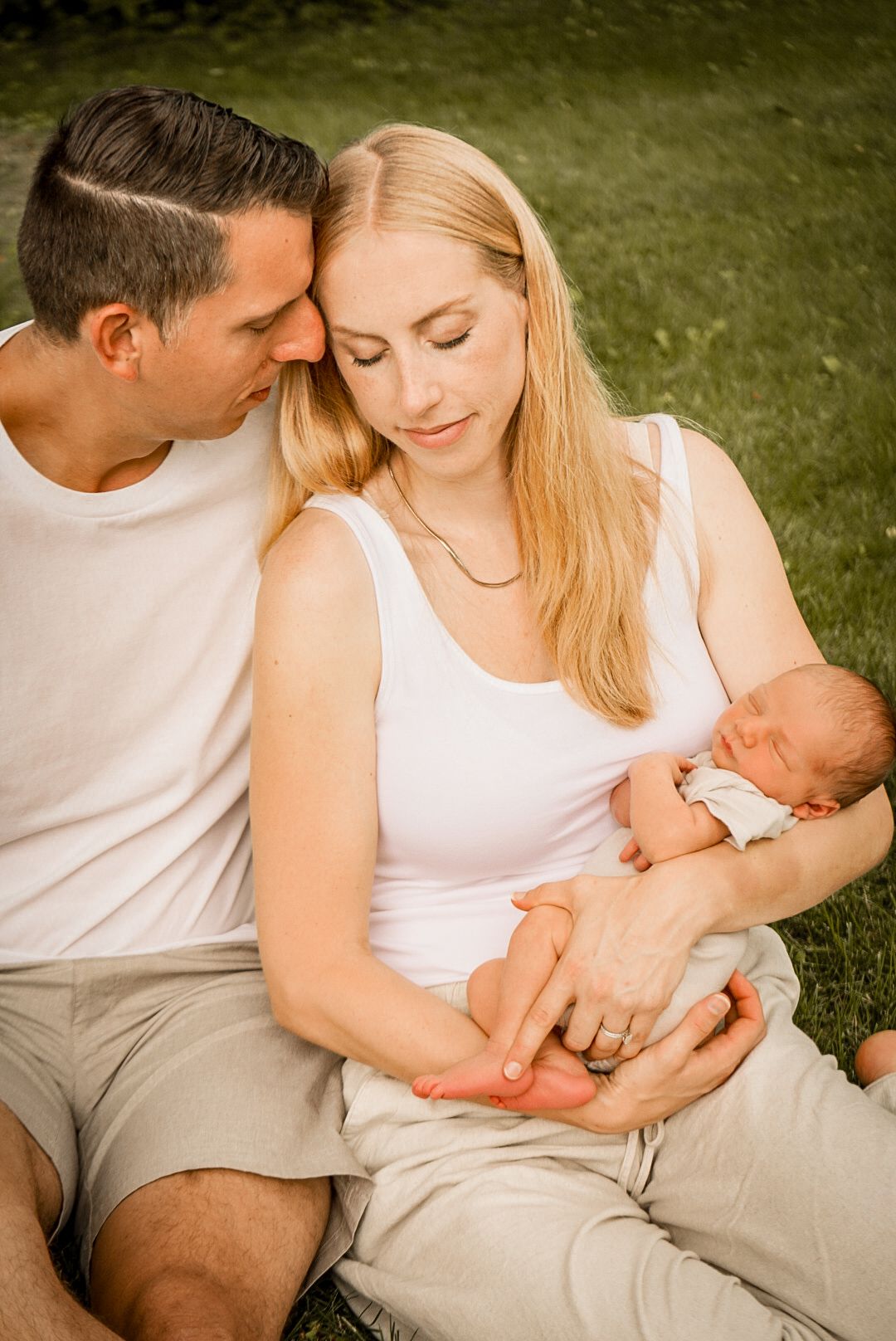 An intimate outdoor family portrait showing parents bonding with their newborn baby.