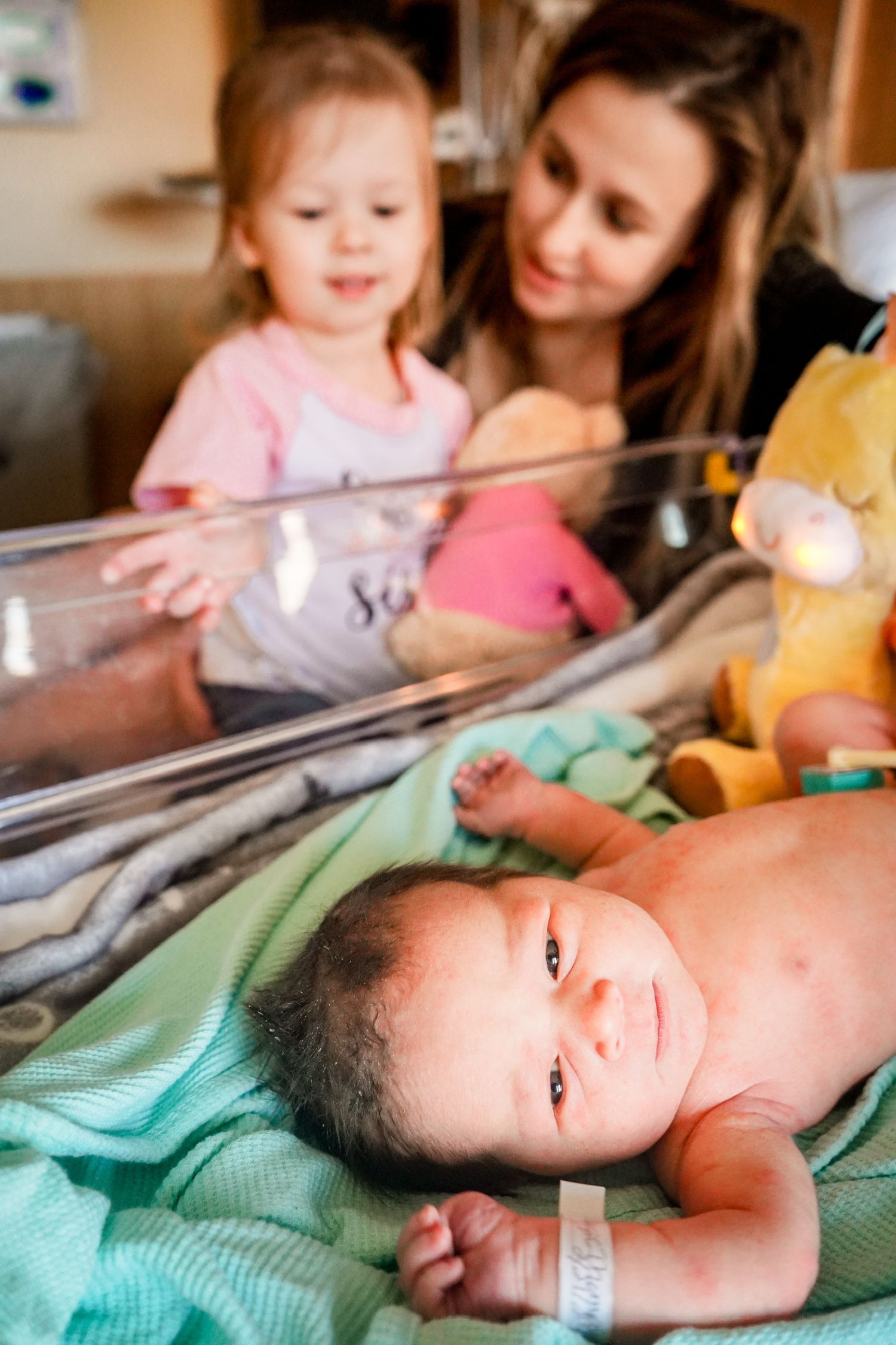 Newborn baby rests on teal blanket while being monitored in hospital setting.
