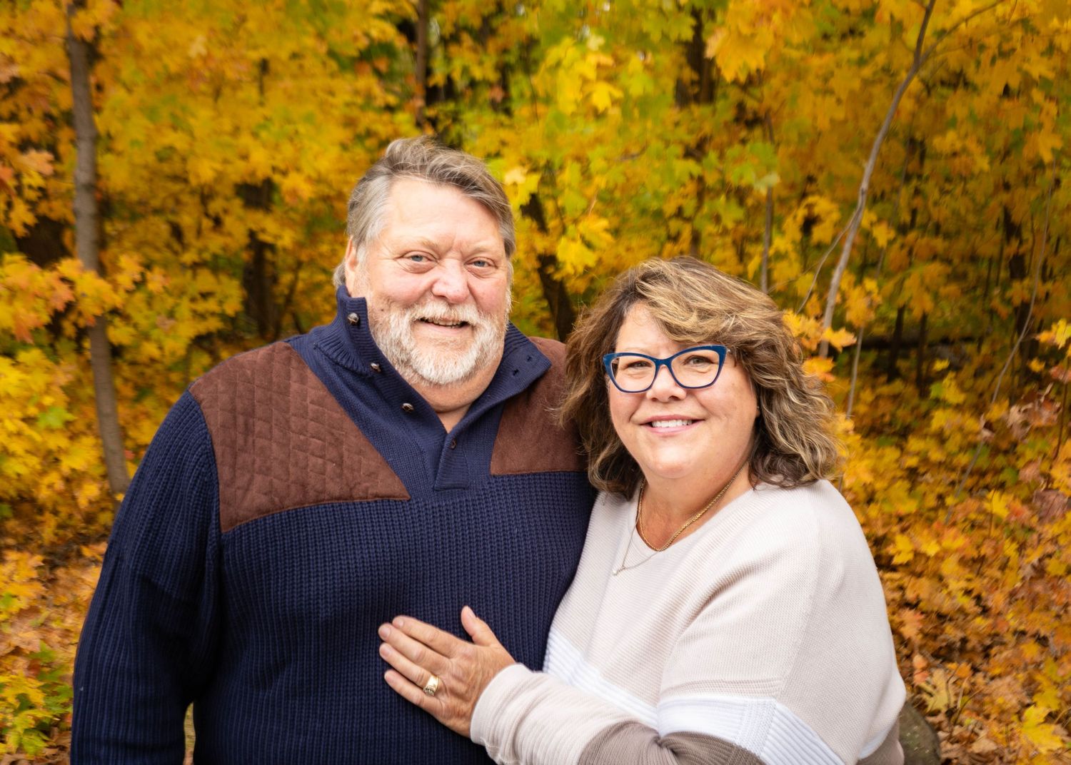 Couple laughing together outdoors during autumn with vibrant yellow foliage in background.