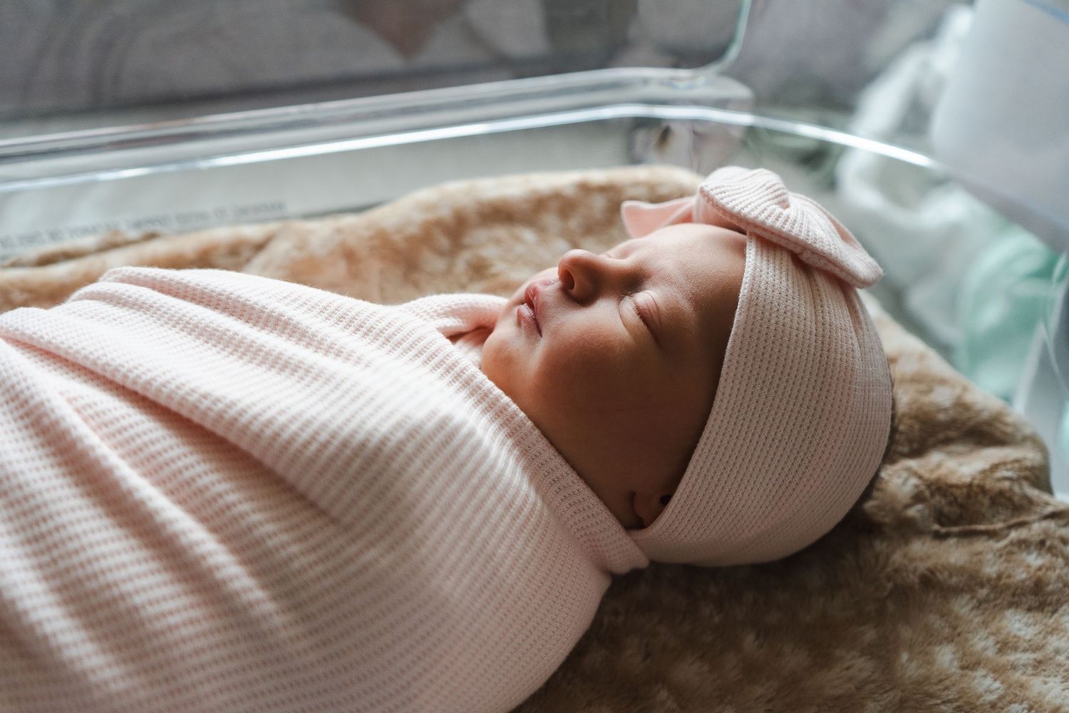Newborn baby sleeping peacefully on soft textured blanket in muted neutral tones.