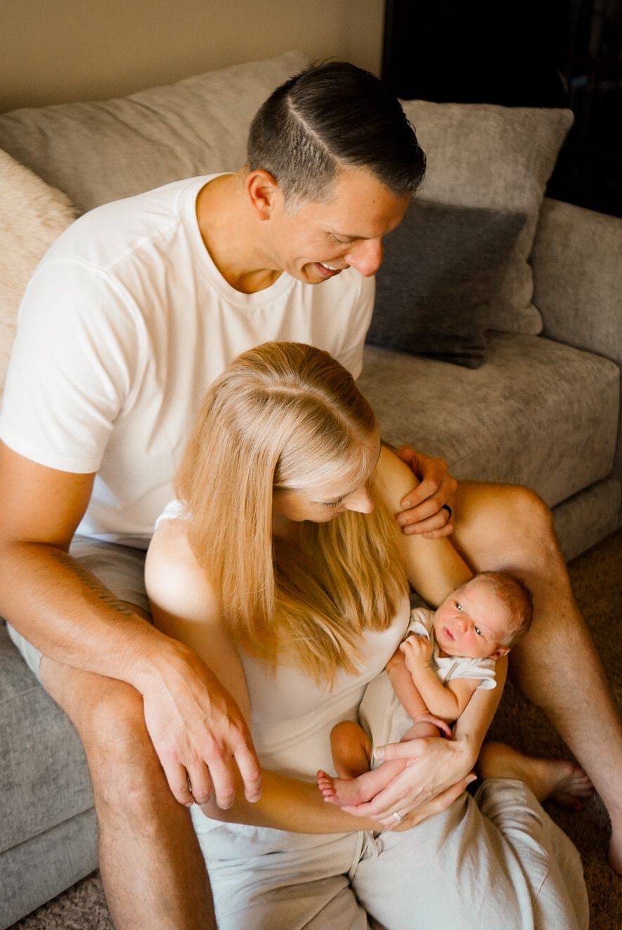 Tender moment between parents and newborn baby during home photoshoot.