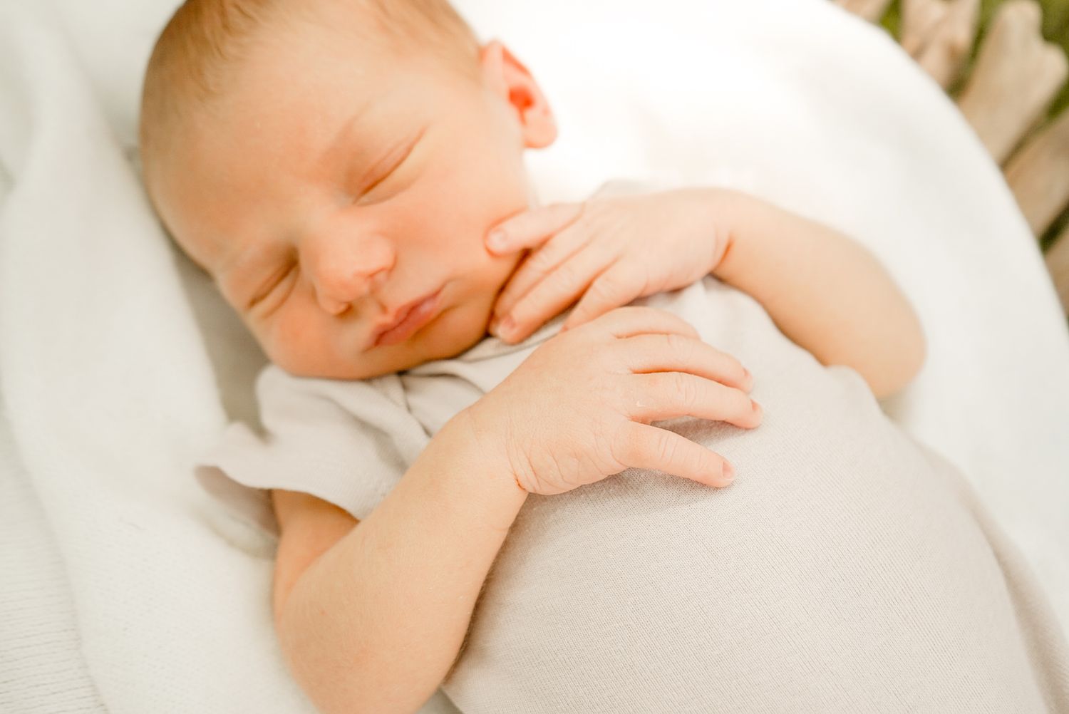 Gentle closeup of sleeping newborn in light clothing against pure white bedding.