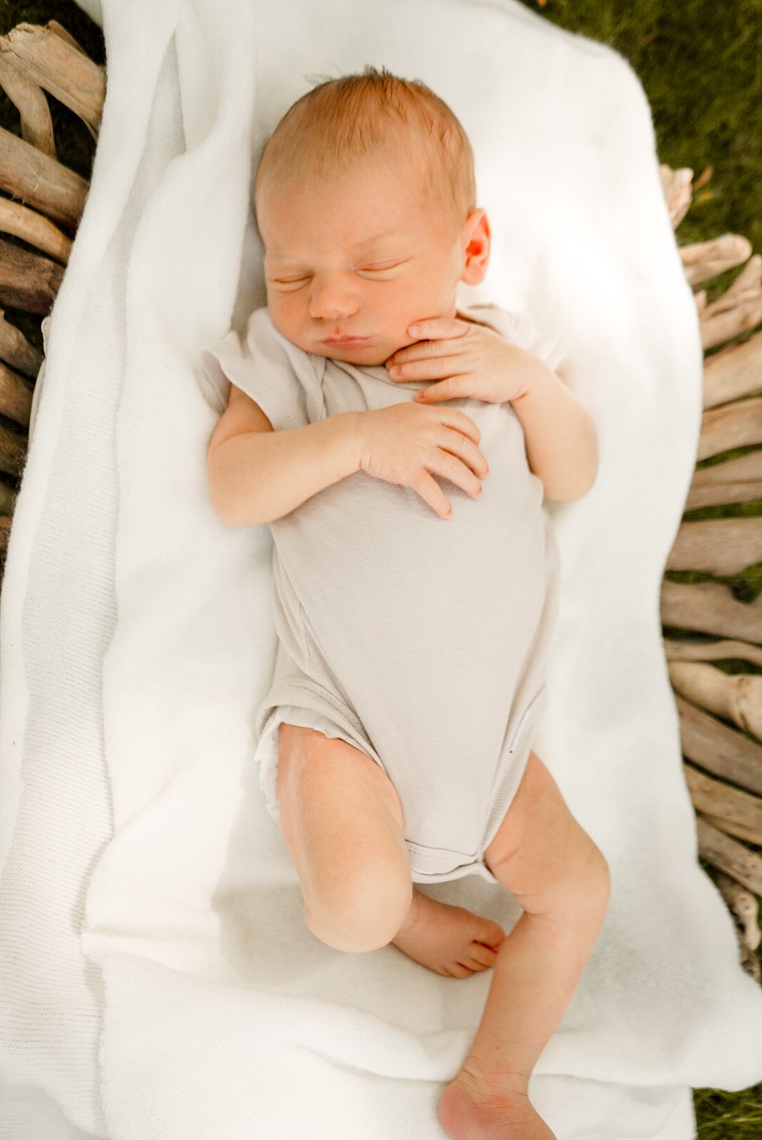 Sweet newborn baby resting on soft white blanket outdoors with wooden textures visible underneath.