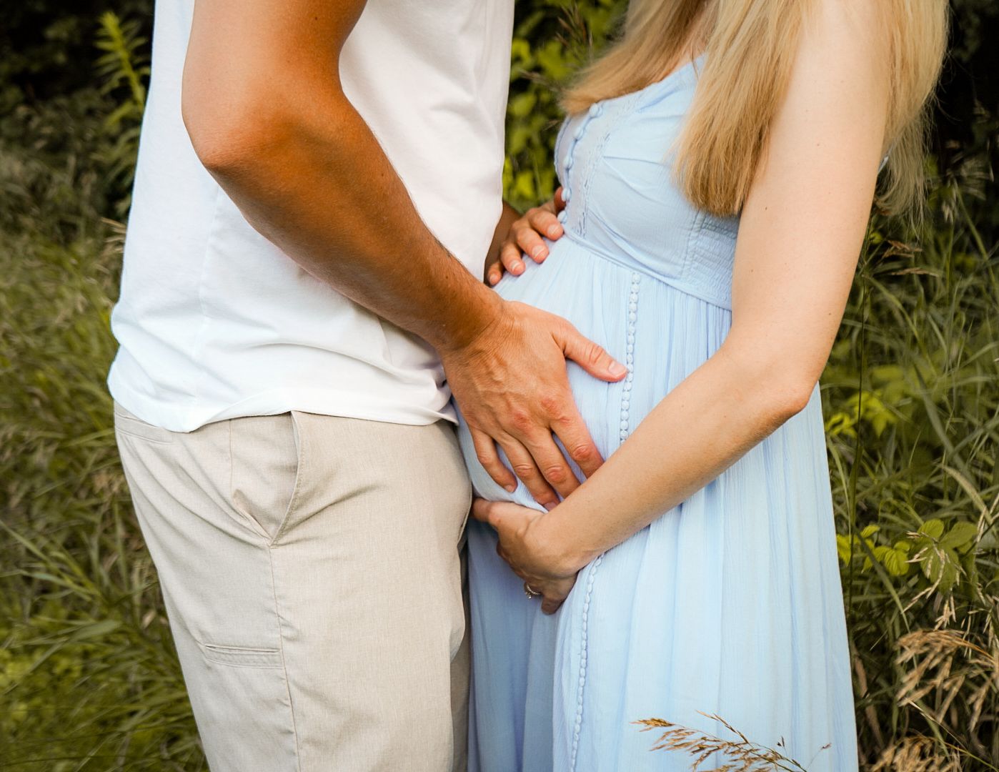 Couple embraces while standing in a grassy outdoor area during a warm sunny day.