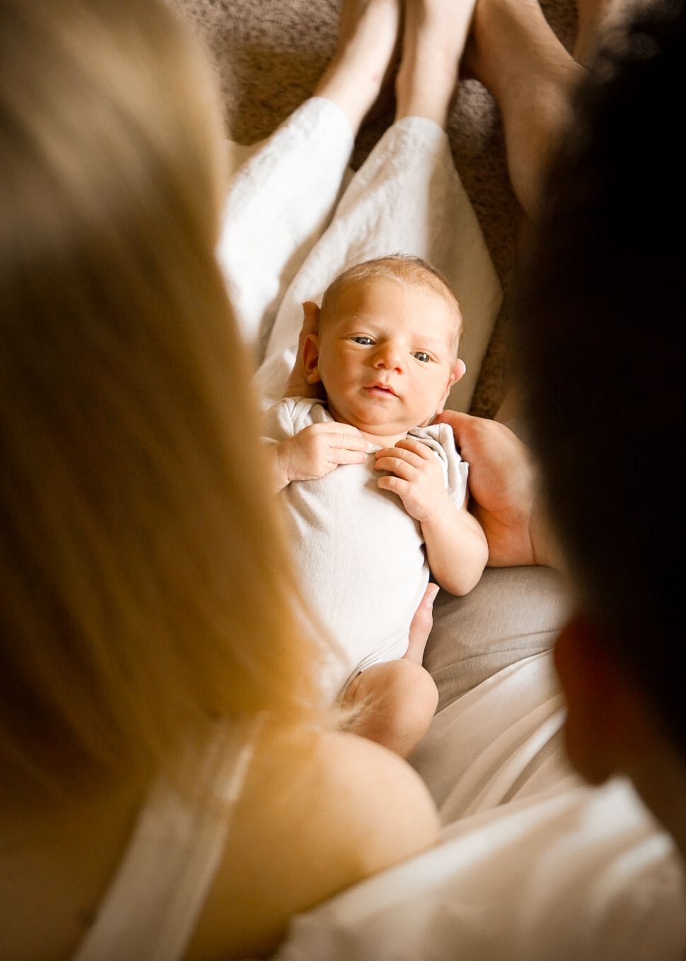 A newborn baby rests peacefully on white bedding in a warm, intimate setting.
