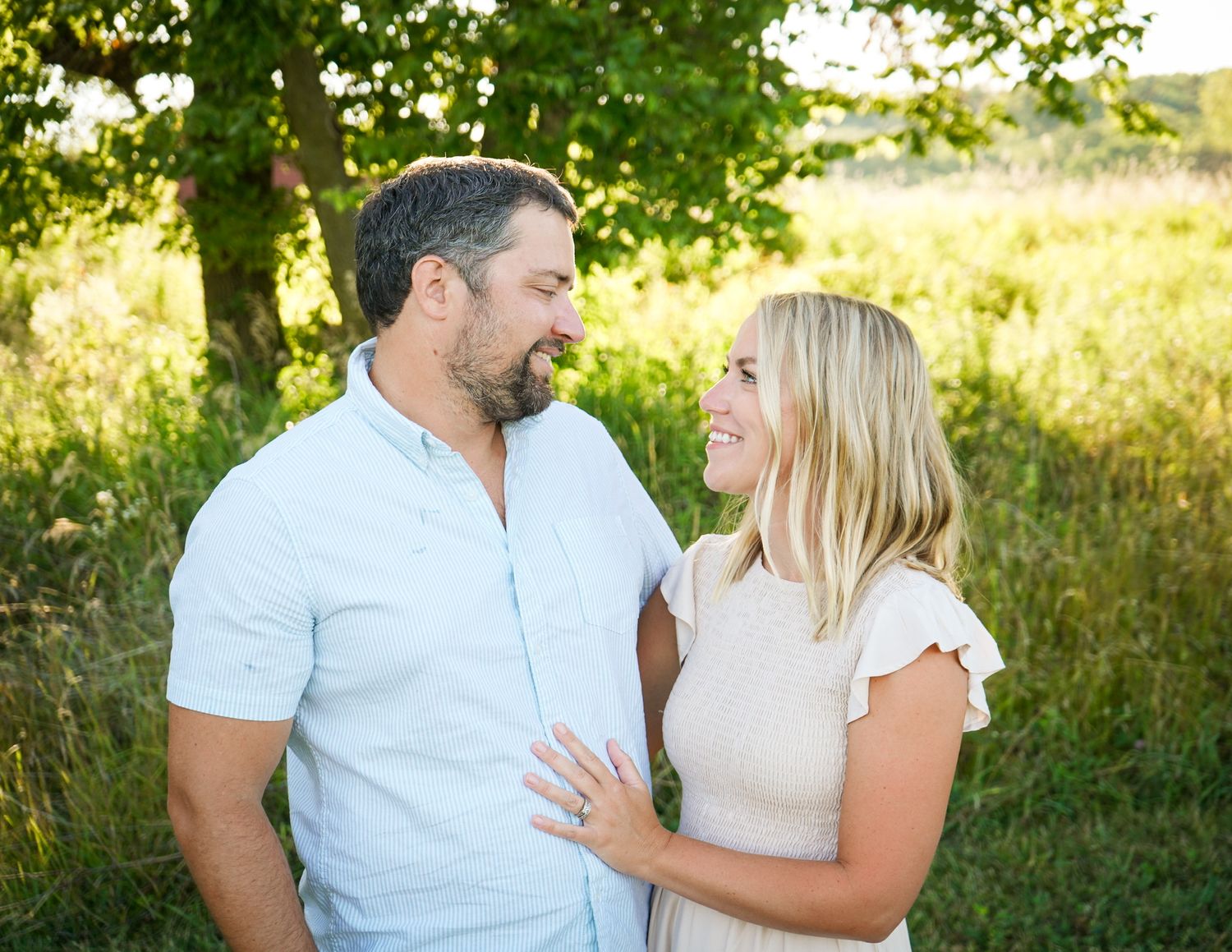 Couple enjoying a romantic outdoor photoshoot in a sunlit meadow with green foliage.