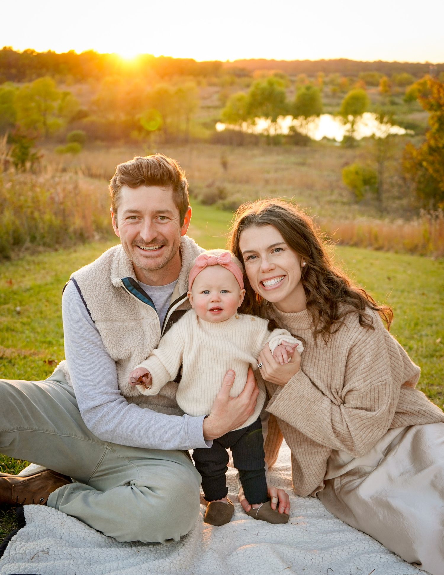 Family lounging together on blanket during golden sunset on grassy hillside.