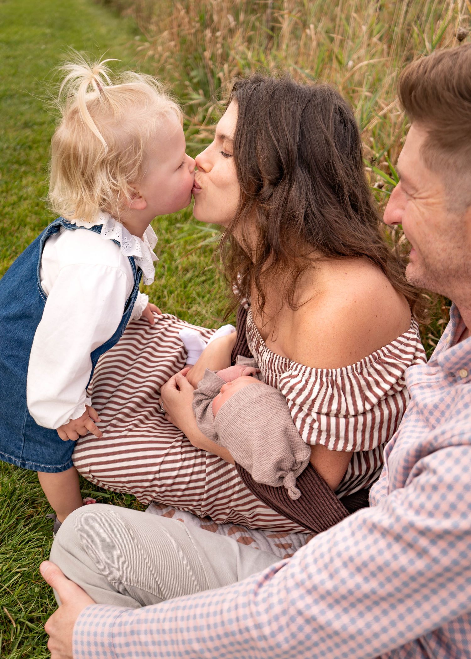 Family enjoying an intimate outdoor moment together on grass with coordinated casual outfits.