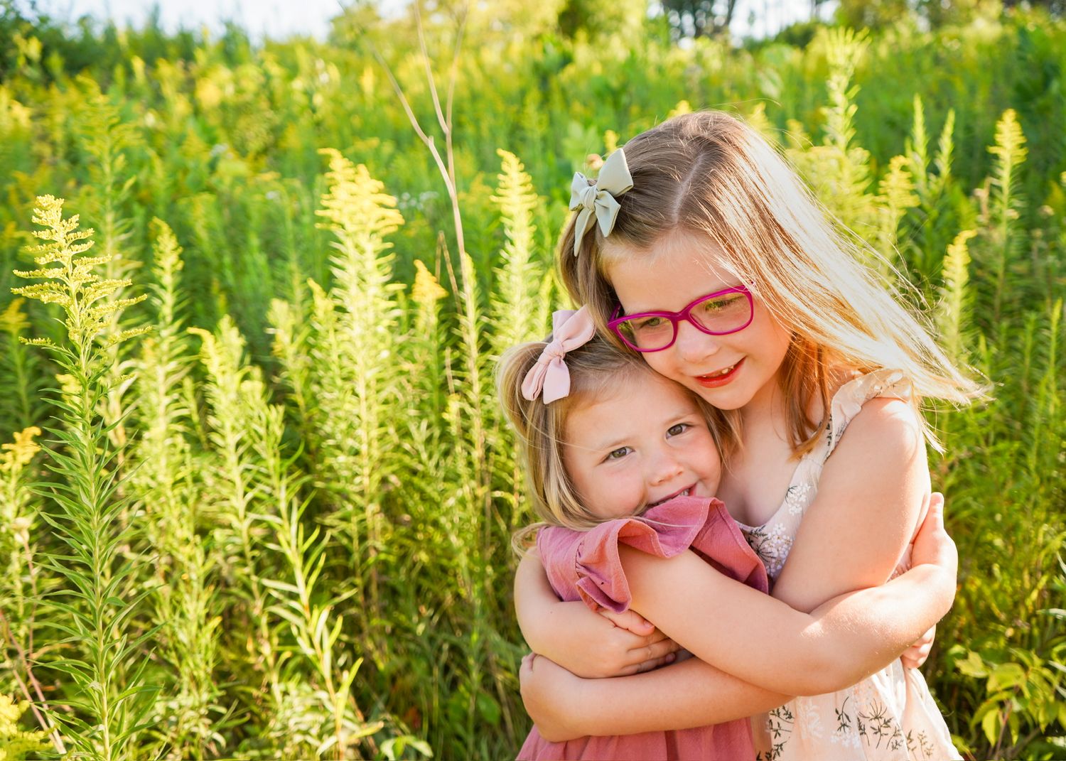 Two children embracing and laughing together in a field of tall yellow summer flowers.