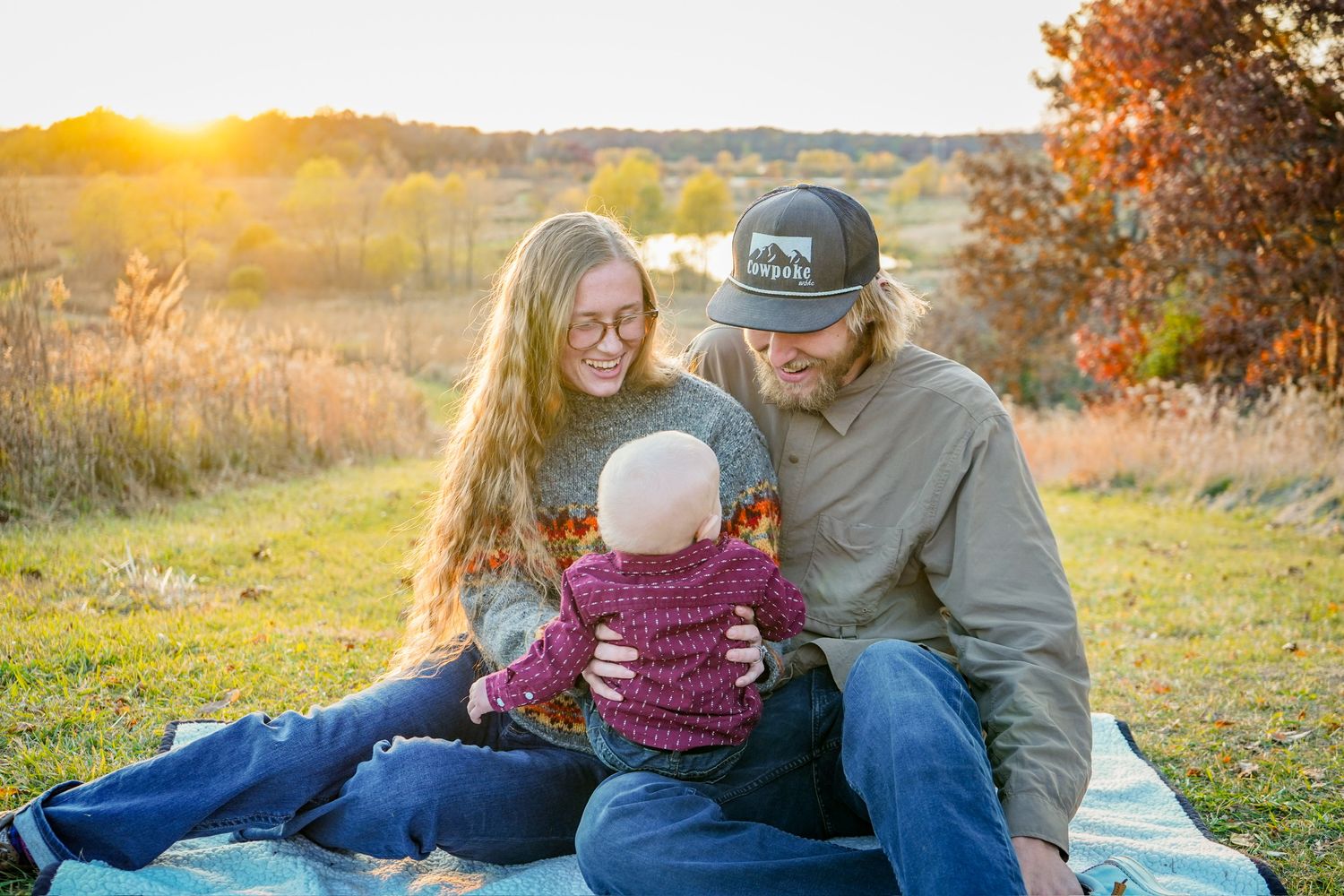 Family embraces during golden hour sunset in autumn field setting.