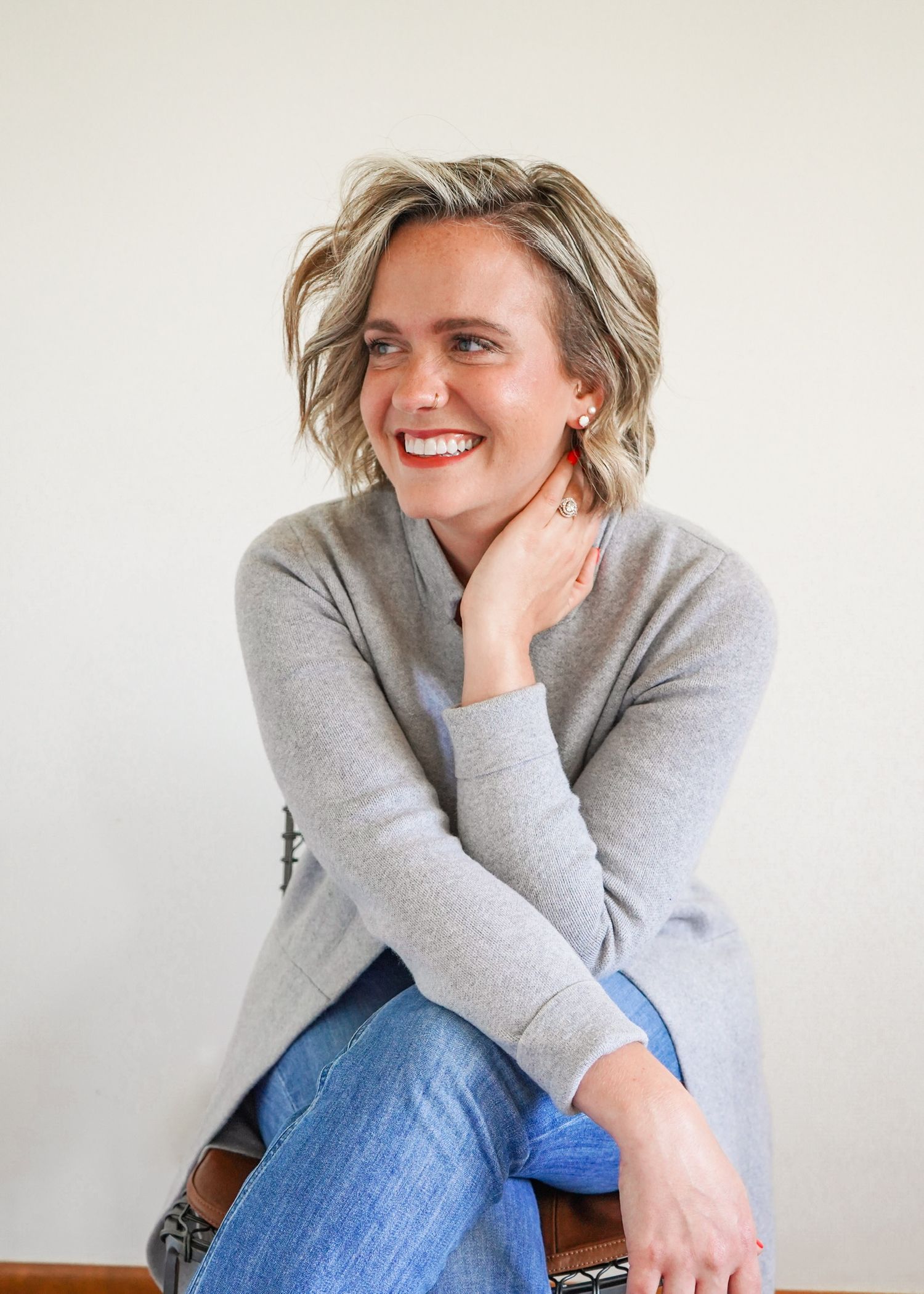 A person in a grey sweater and jeans sits casually while smiling and laughing in a multi-panel photo series.