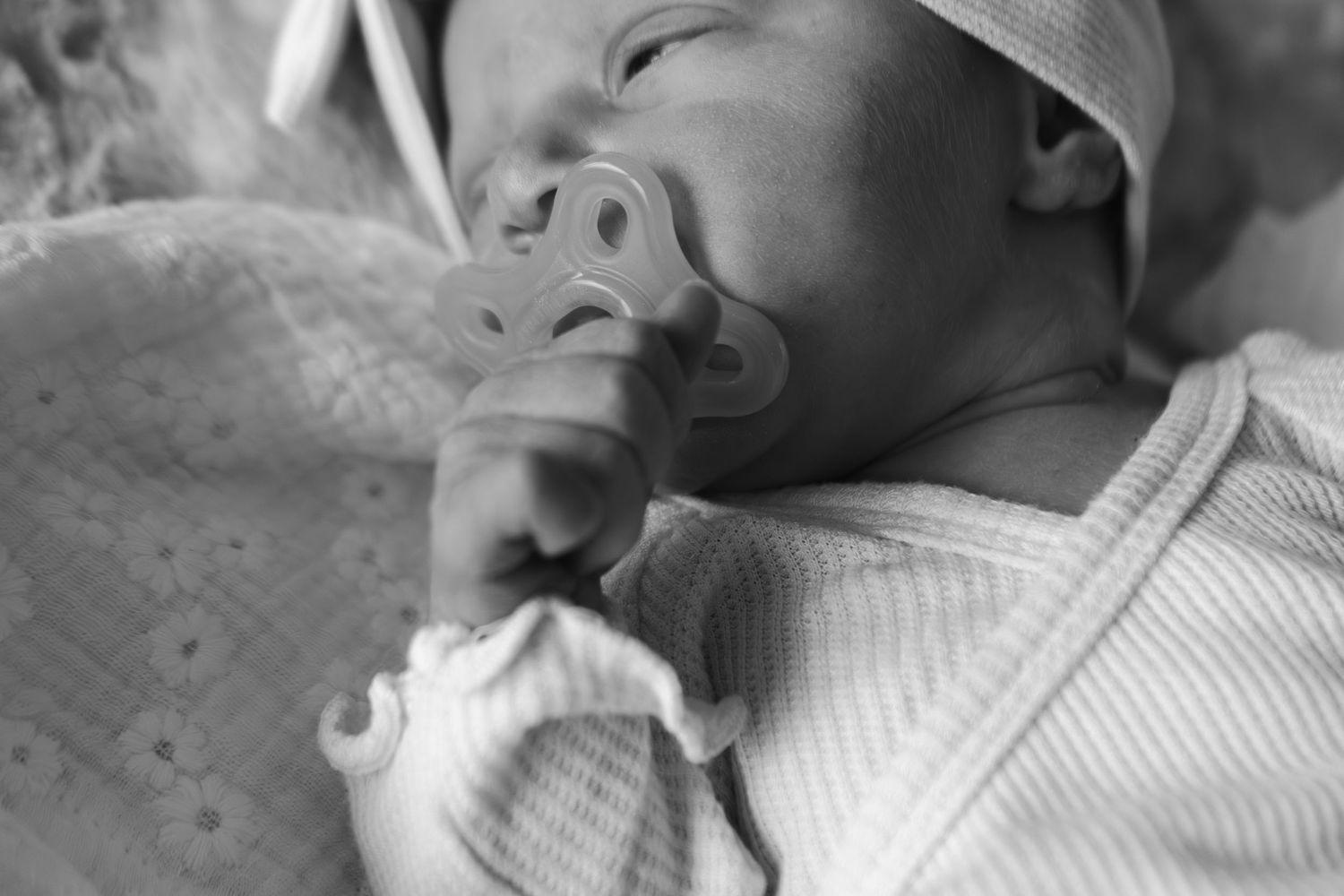 A sleeping baby wearing a white knit outfit rests peacefully on a soft surface.