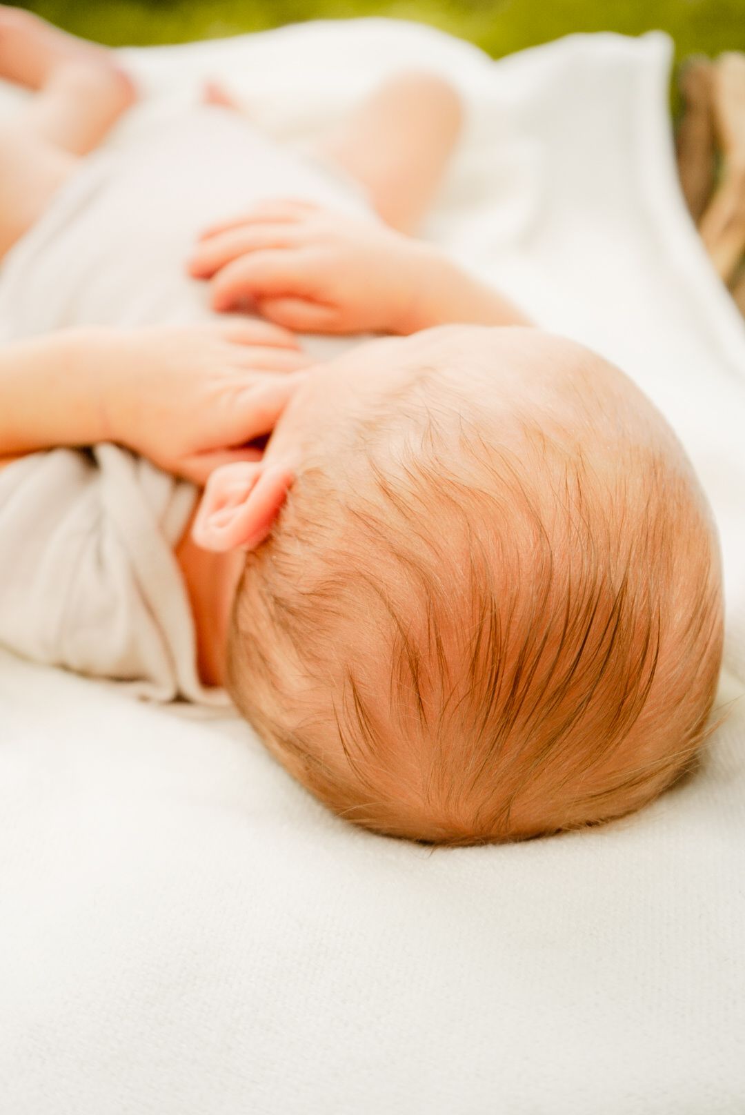 Side view of sleeping newborn on white blanket against green background.