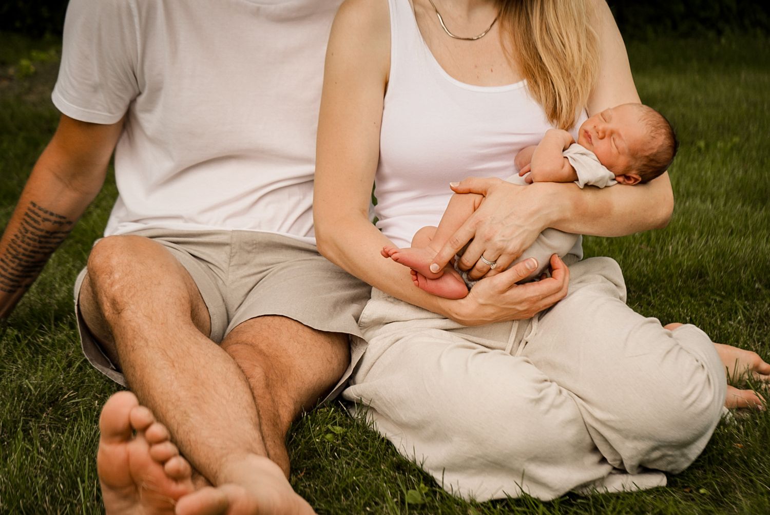 A sweet outdoor family portrait showing a couple with their newborn baby on the grass.