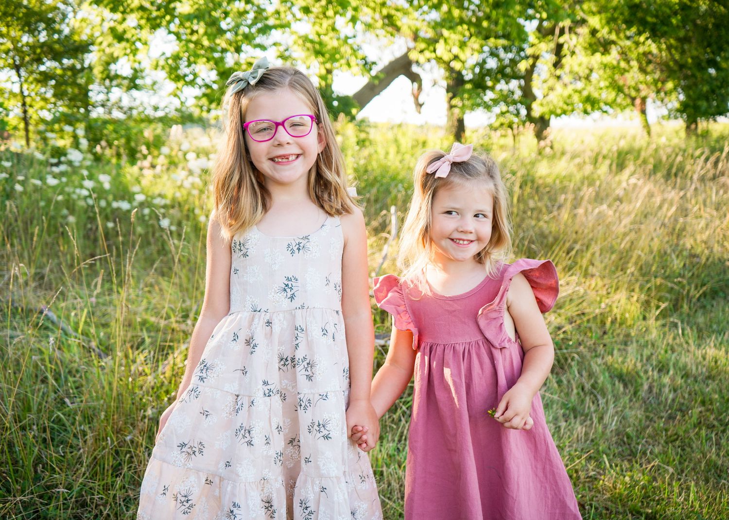 Two children in pretty dresses standing together in a sunlit summer field.