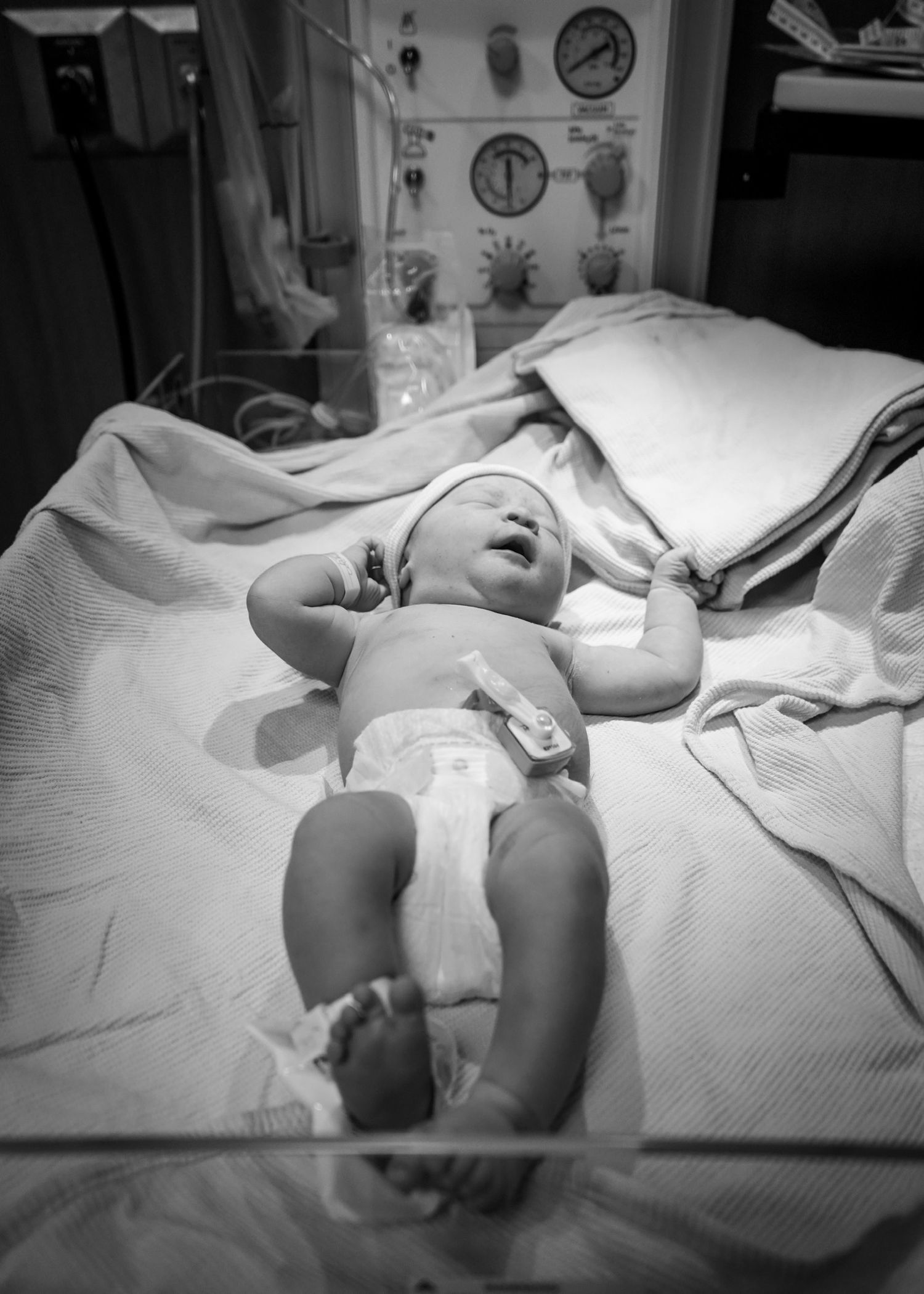 Medical scene showing a newborn on examination table in monochrome.