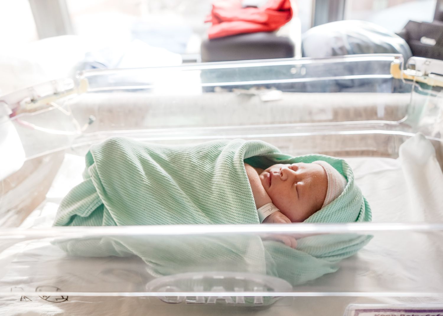 Newborn baby sleeping peacefully in hospital bassinet with mint green blanket.