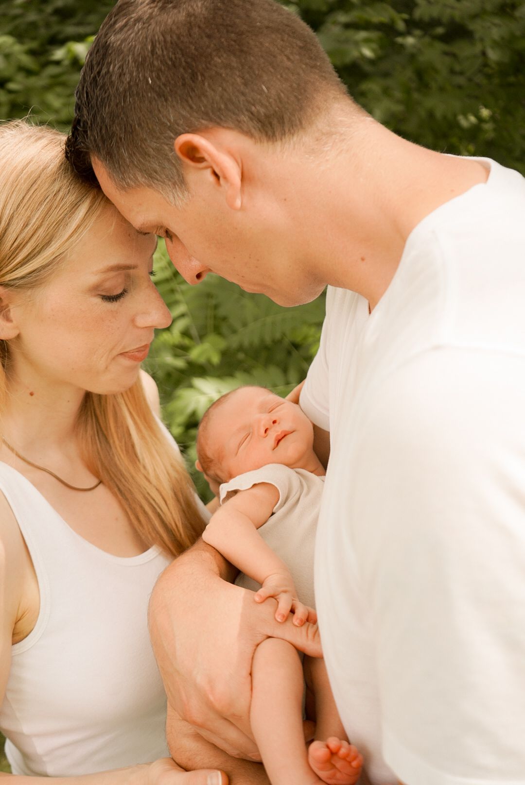 Intimate outdoor portrait of a couple sharing a tender moment with their newborn baby.