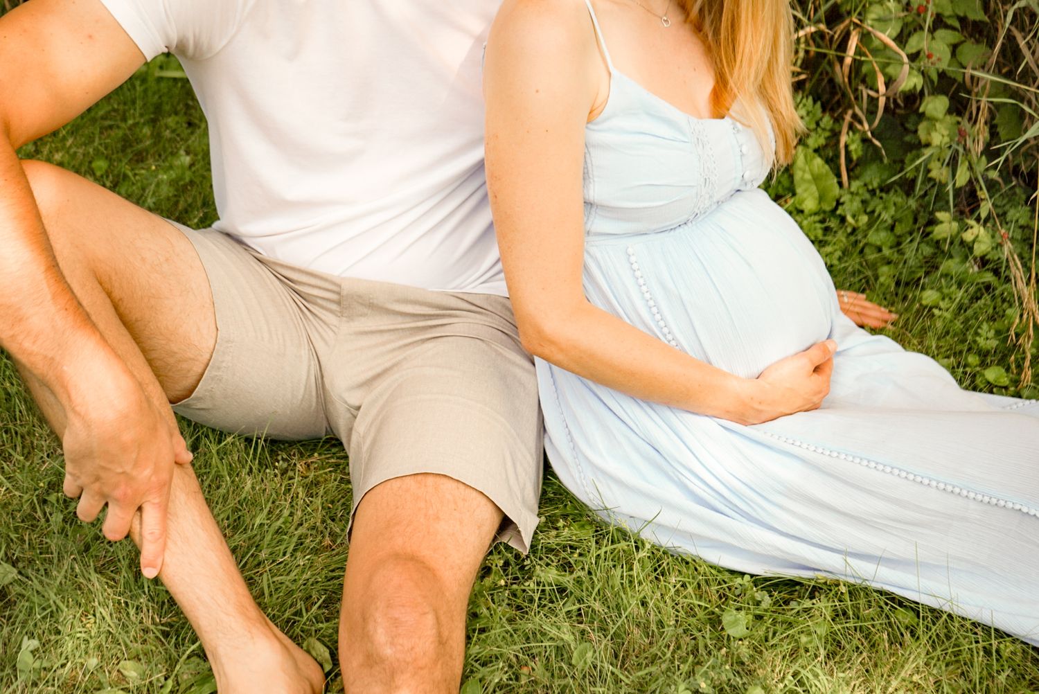 Couple sits together on grass wearing casual clothing during maternity photoshoot.