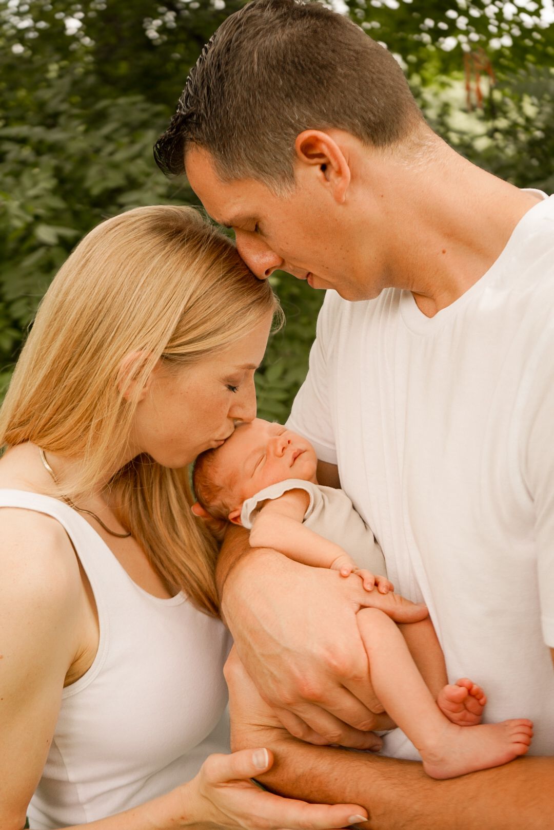 Artistic series showing tender family moments with newborn baby in natural outdoor setting.