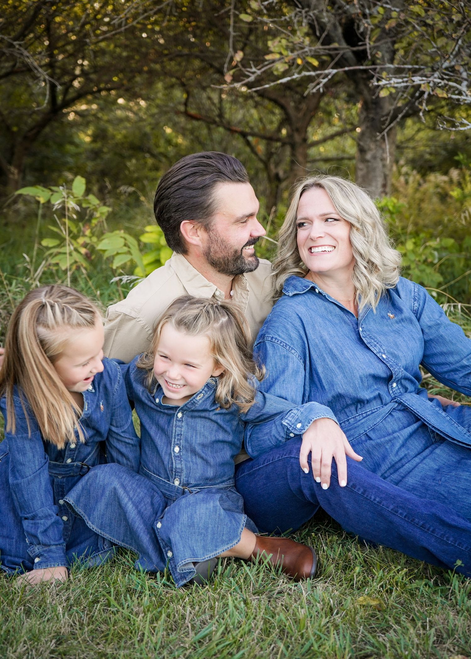 Family relaxing on grass wearing matching denim outfits during outdoor photo session.