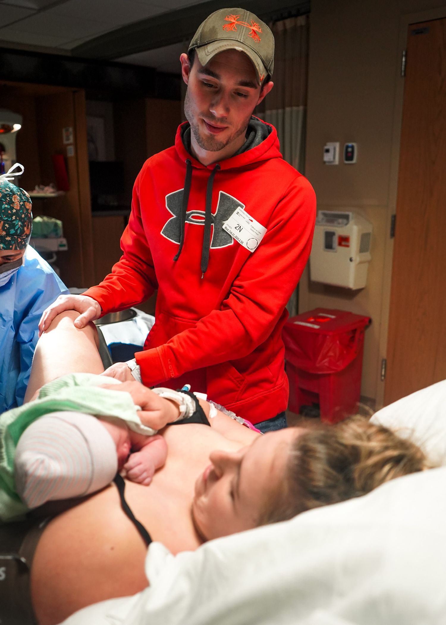 Healthcare worker in red sweatshirt provides medical care to patient on examination table.